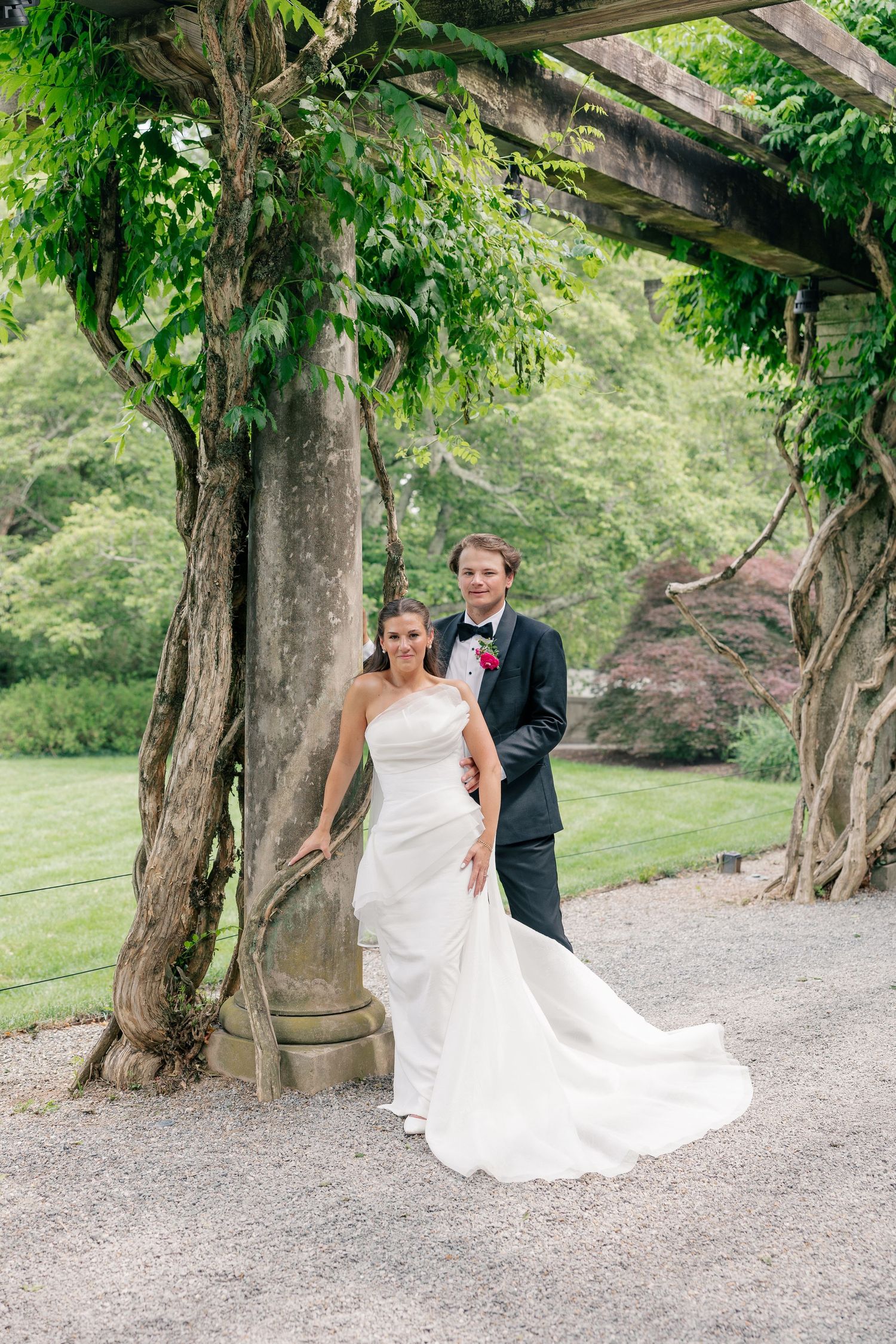Bride and groom pose under lush green ivy pergola in garden setting on wedding day.
