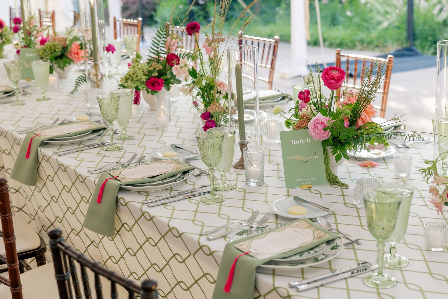 Elegant wedding reception table with geometric linens, pink floral centerpieces, and green glassware.