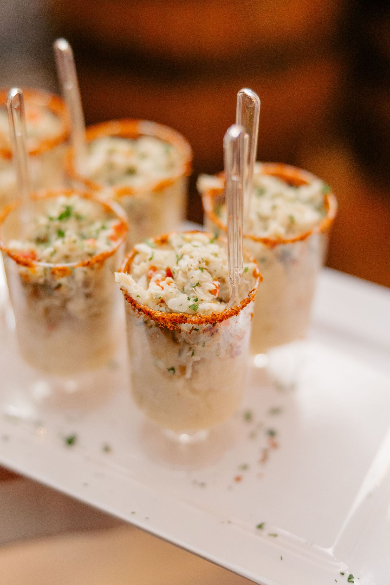 Elegant crab salad appetizers served in spice-rimmed shot glasses with silver spoons on a white tray.