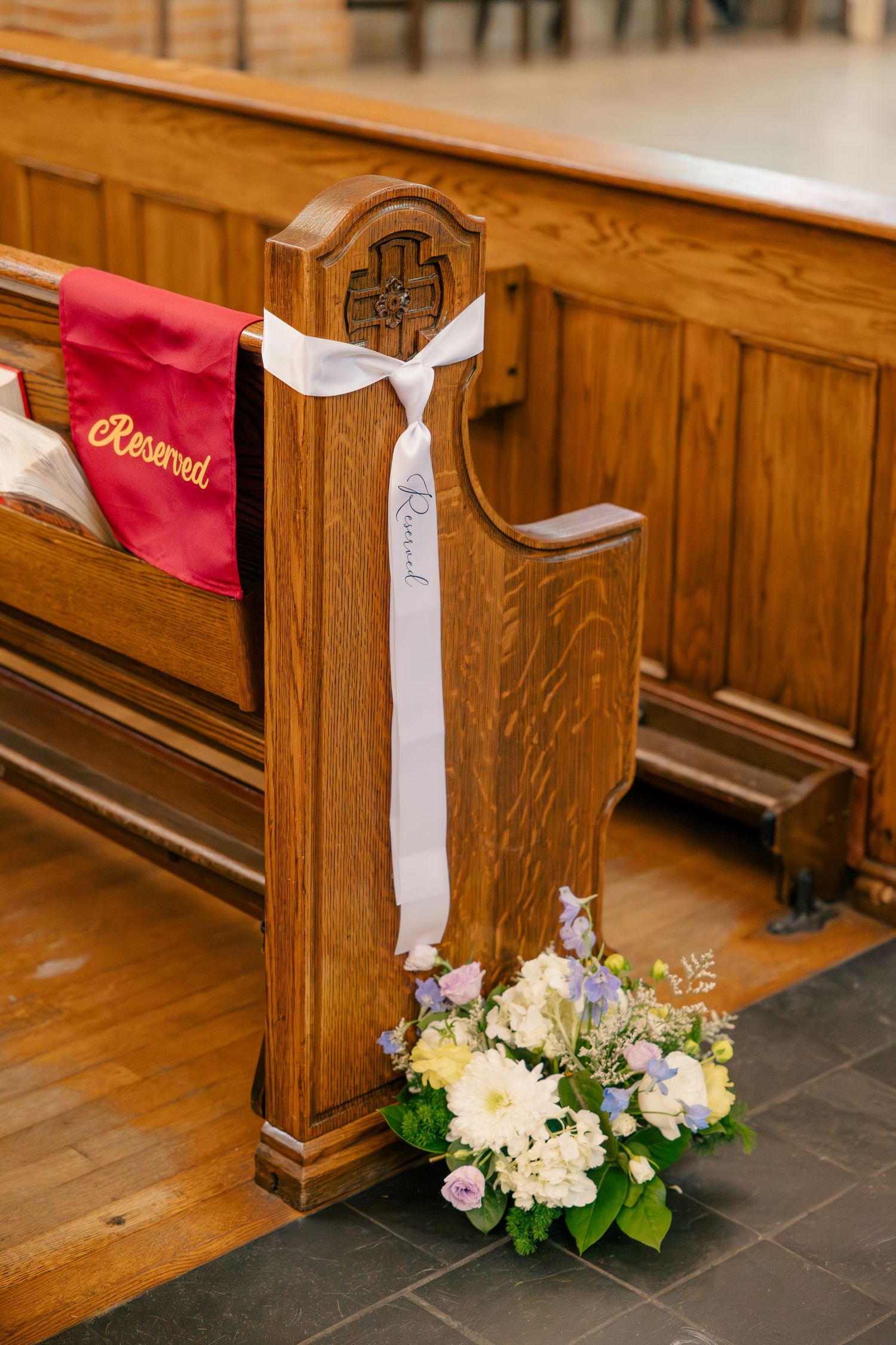 Church pew decorated with white ribbon bow and pastel floral arrangement of white and lavender blooms.
