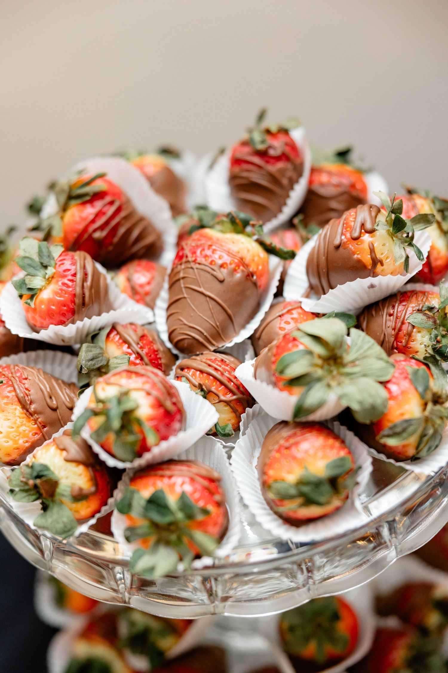 Chocolate covered strawberries garnished with herbs displayed on a crystal serving platter.