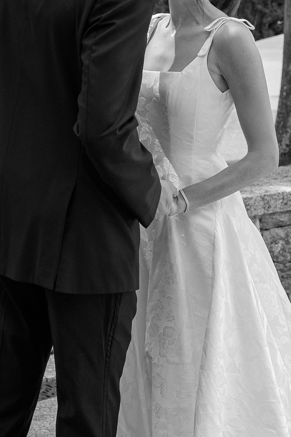 Black and white photo of a bride in white gown holding hands with a groom in dark suit at a wedding.