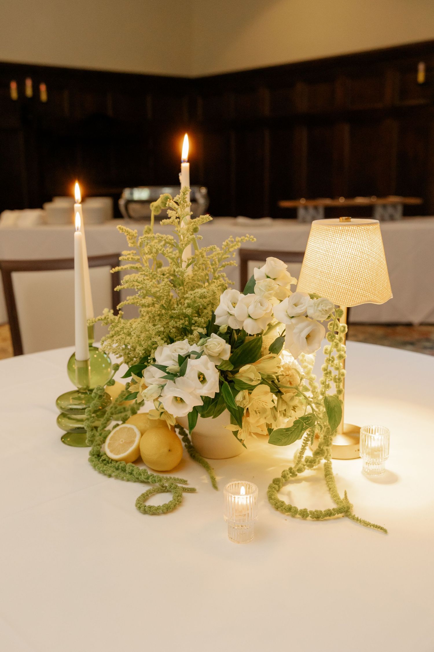 Elegant wedding centerpiece with white flowers, candles, greenery, and lemons on a white tablecloth.