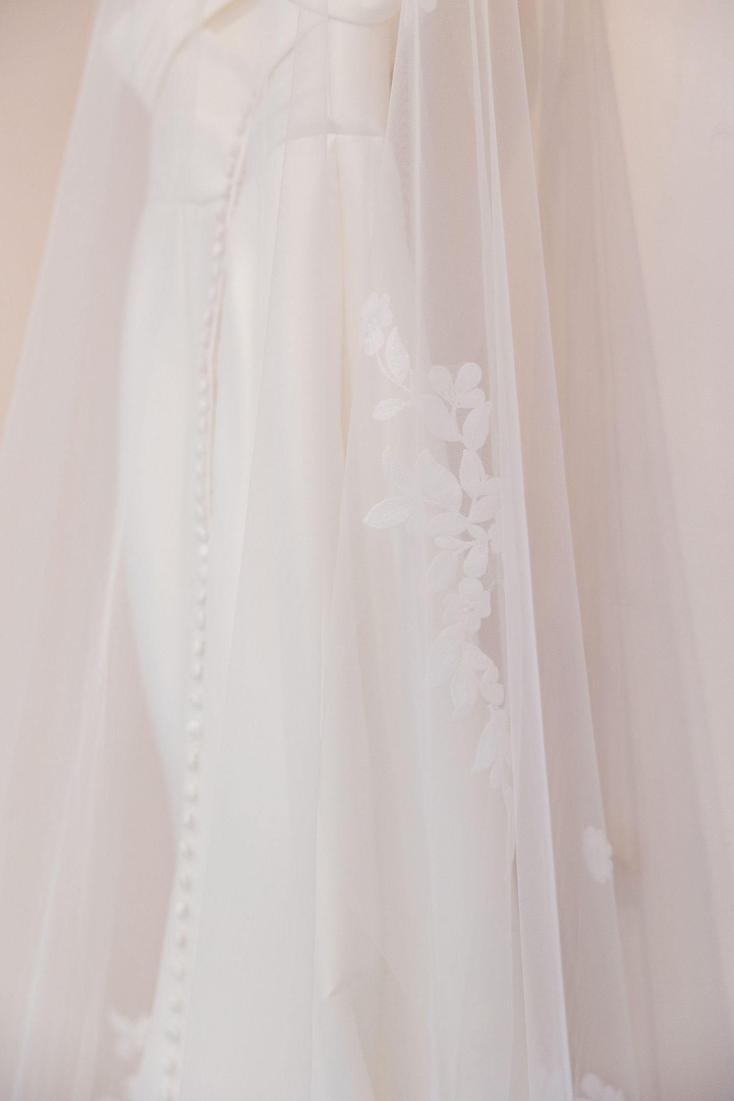 Close-up of an elegant white wedding dress with delicate lace applique veil and pearl button back detail.