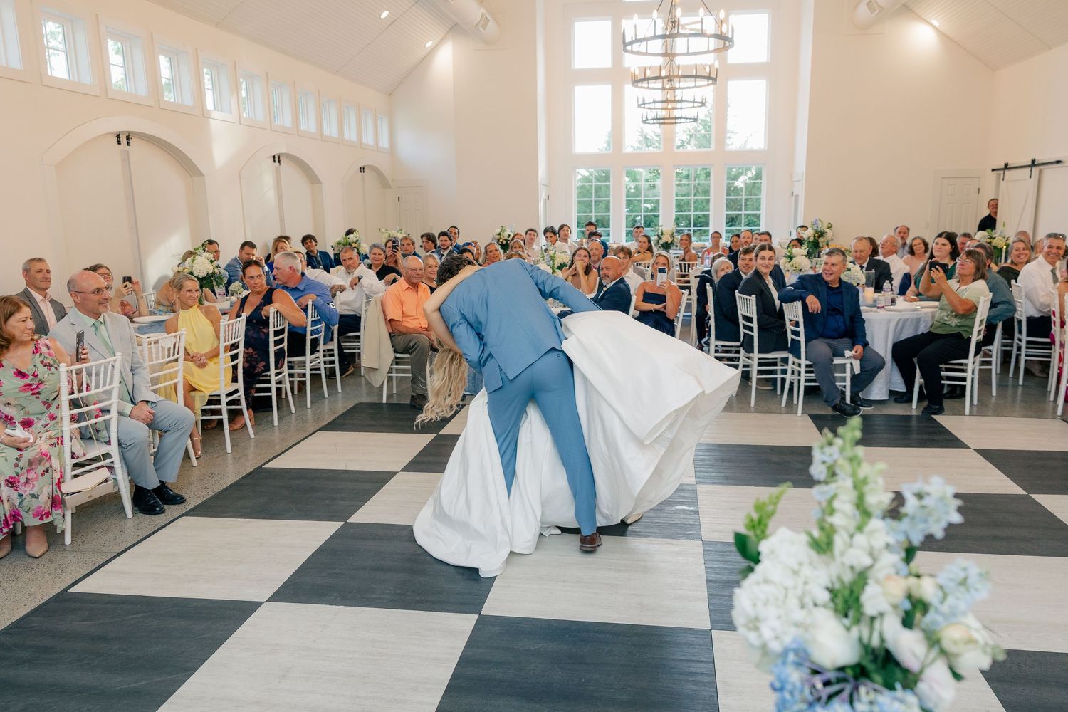 Groom dips bride on black and white checkered dance floor during wedding reception first dance.