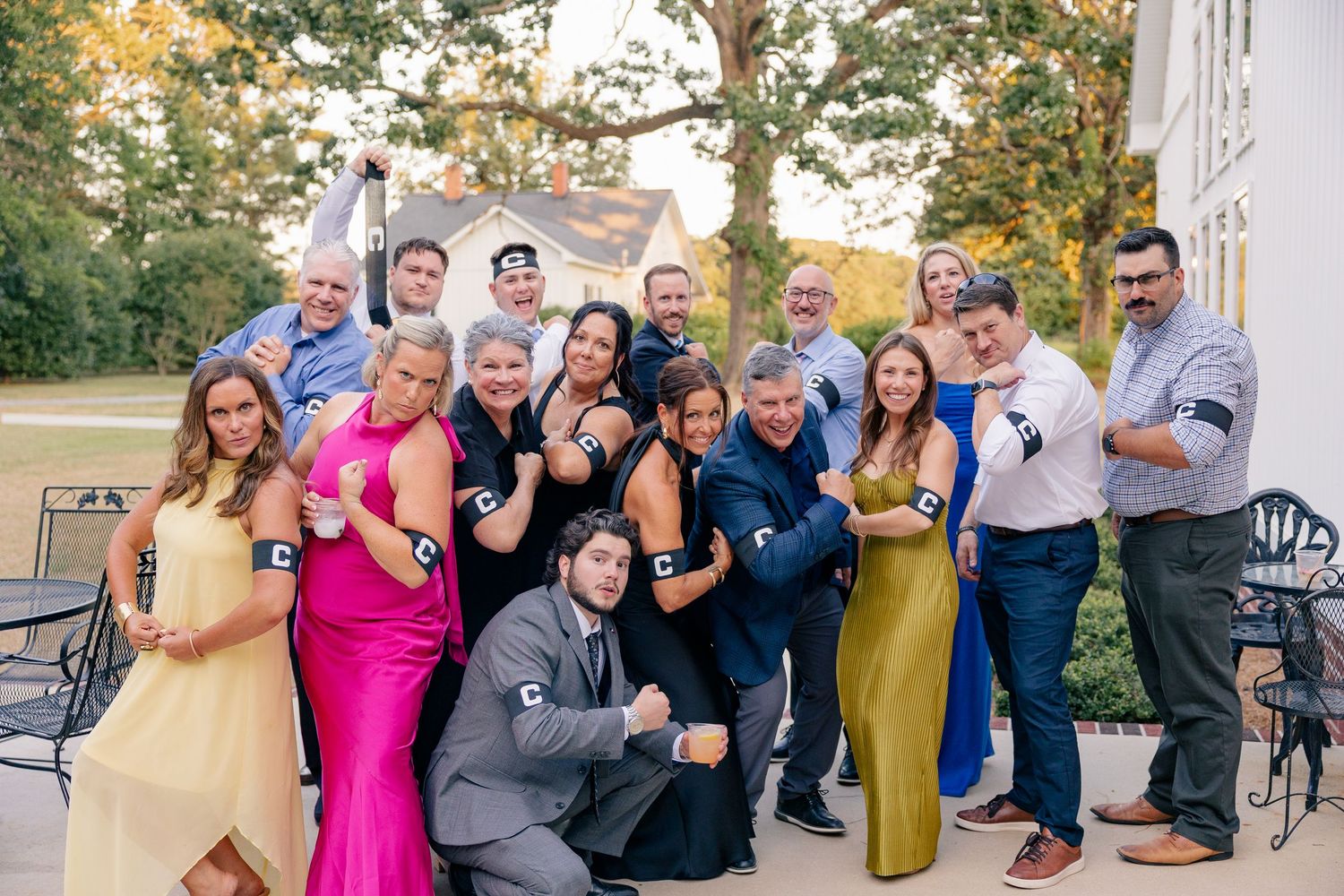 Large wedding party group posing playfully outdoors at a reception venue in formal attire.