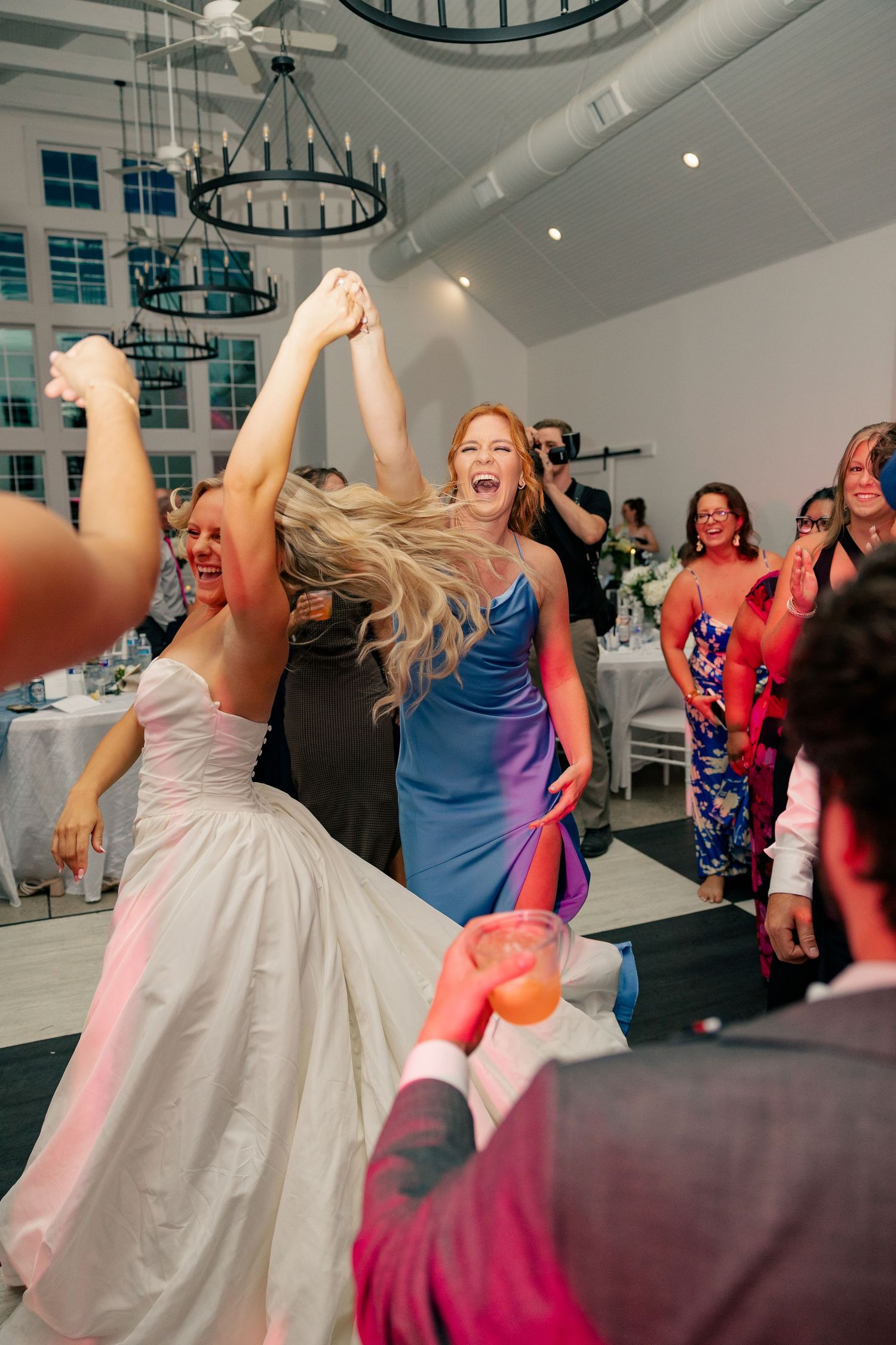 Laughing bride in white gown dances energetically with guests at lively wedding reception.