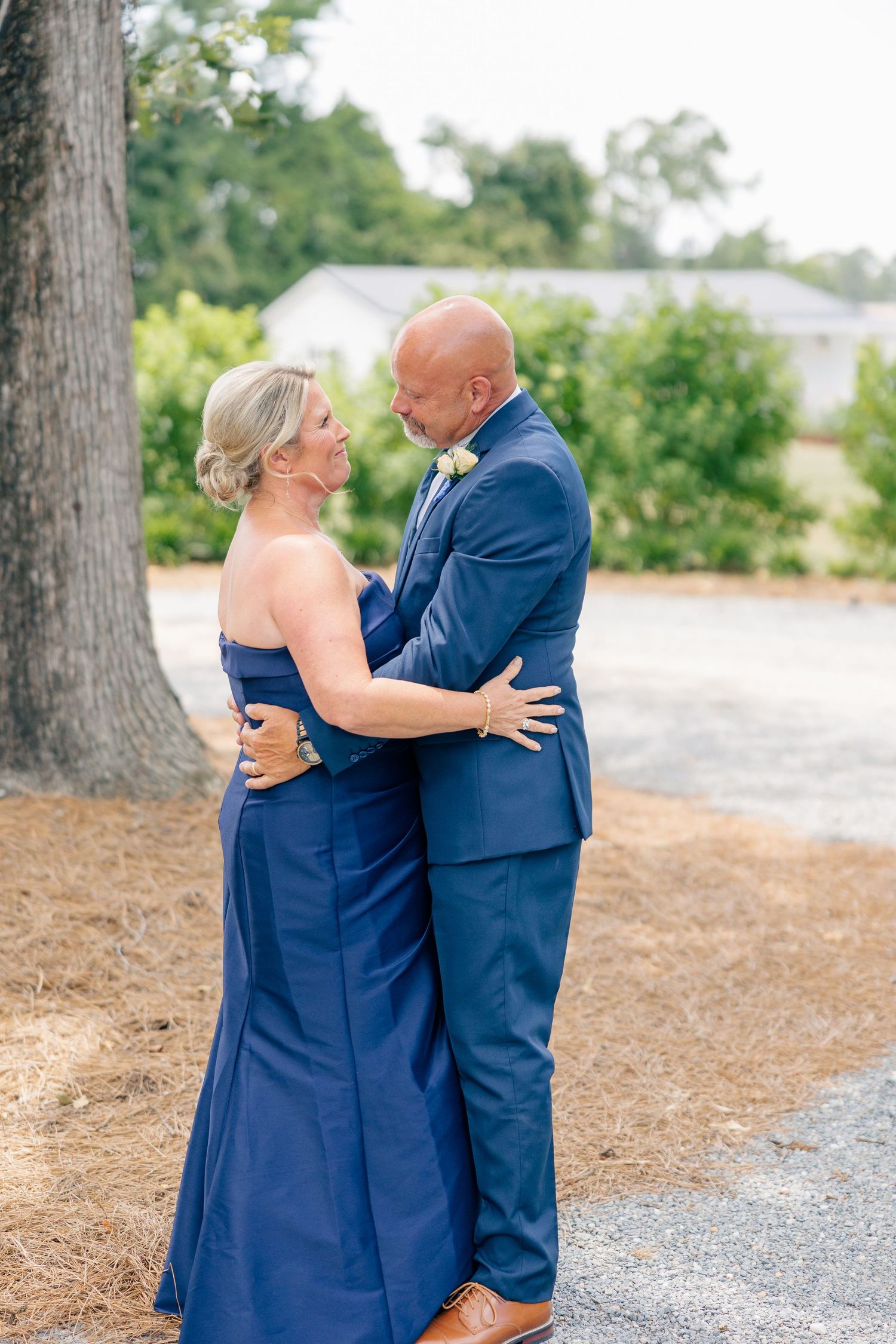 Elegant couple in navy attire smiling and embracing outdoors at a wedding venue.