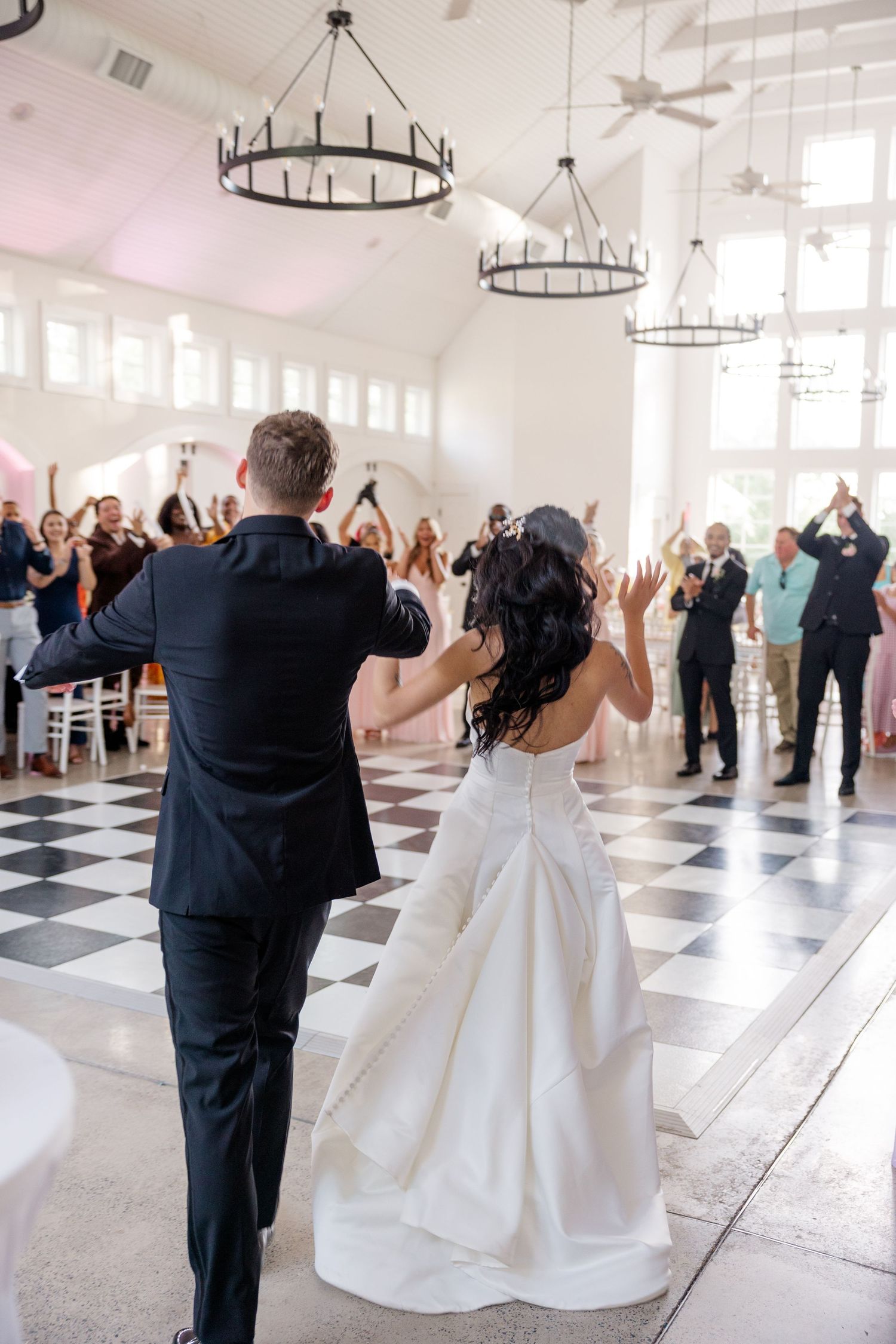 Couples dancing energetically in a modern white reception venue with checkerboard floor.