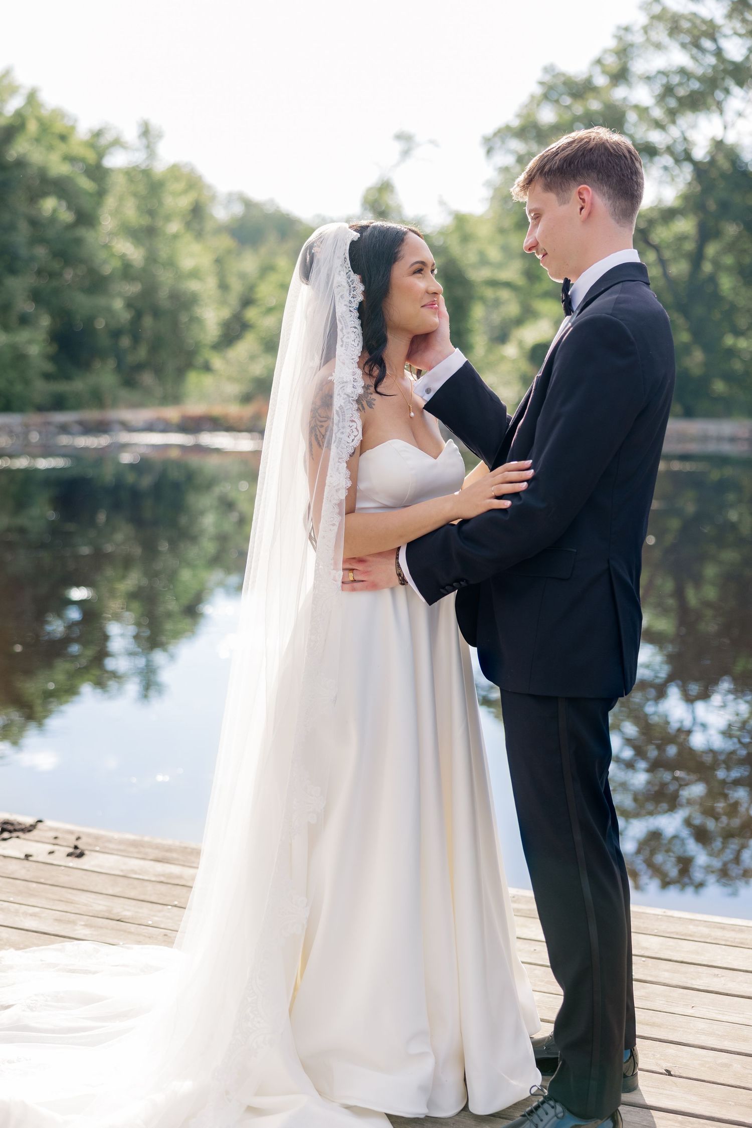 Romantic wedding couple embraces on wooden dock by scenic lake.