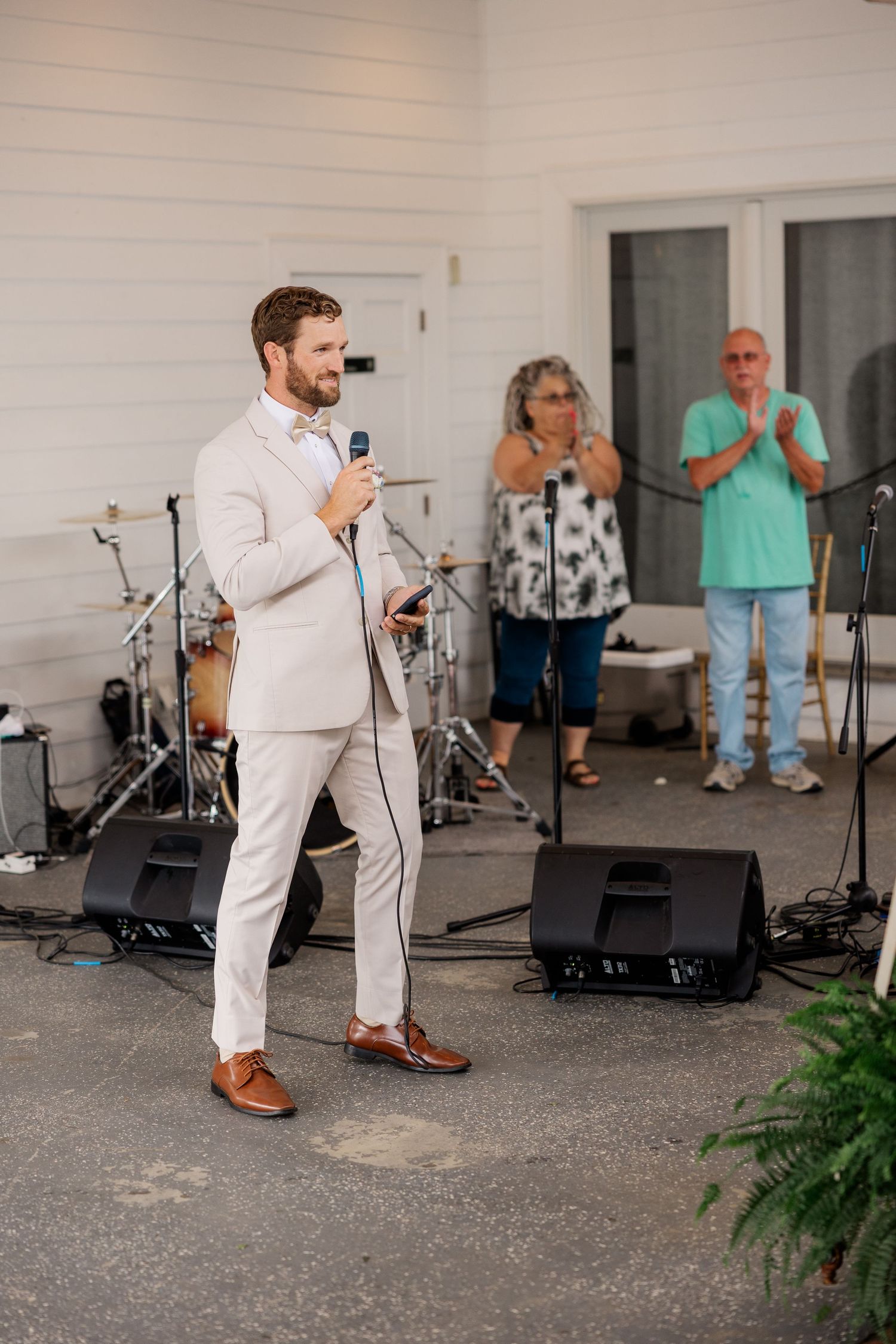 A performer in a light suit sings into a microphone on an outdoor stage.