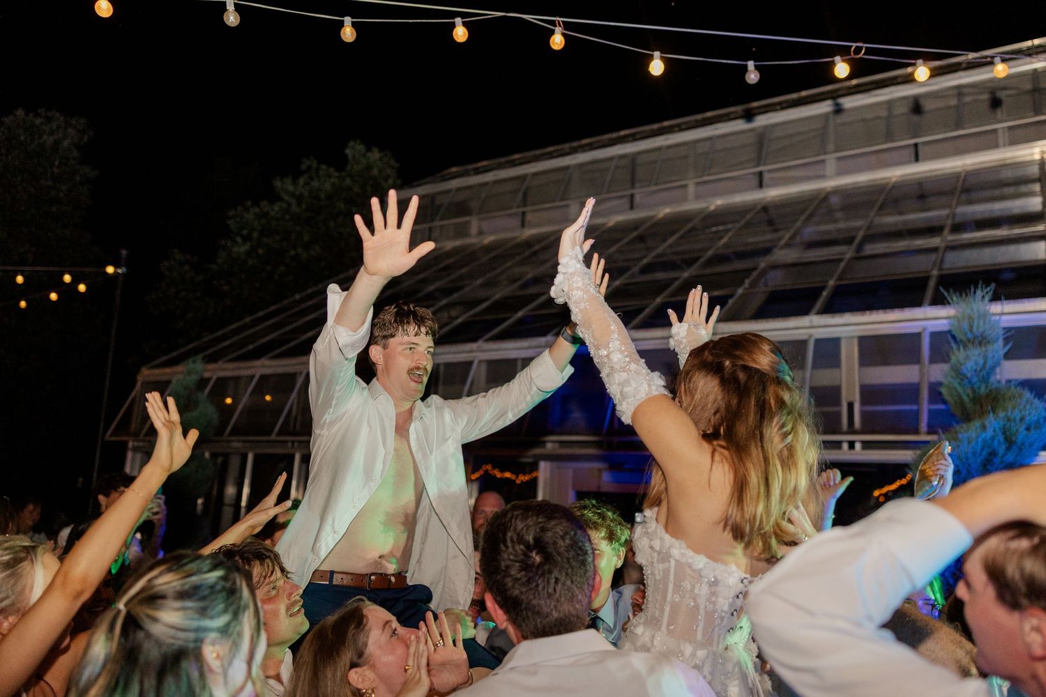 Energetic wedding reception scene with string lights and celebration on the dance floor.