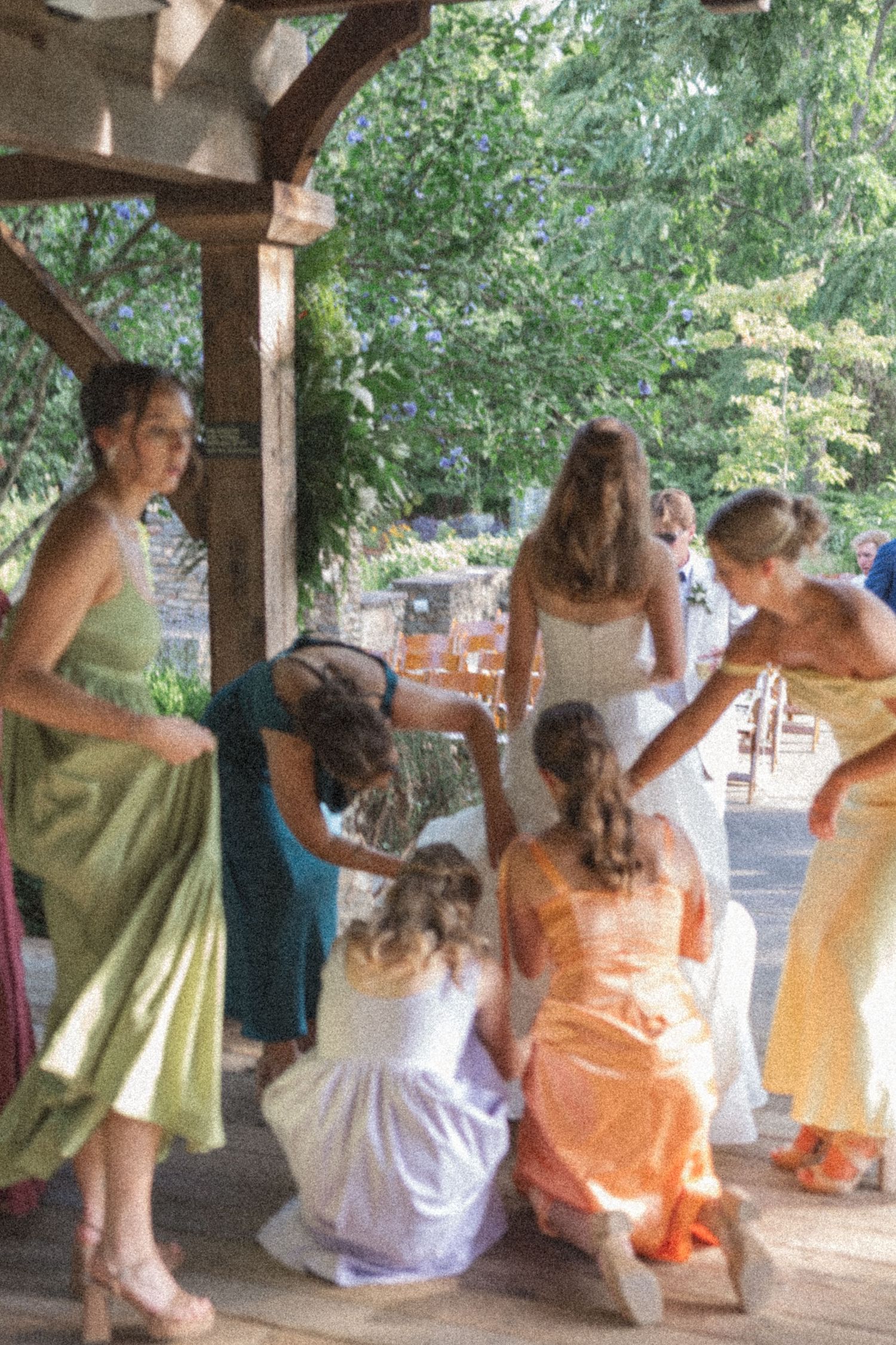 A group in colorful dresses gather under a wooden pergola during a special occasion.