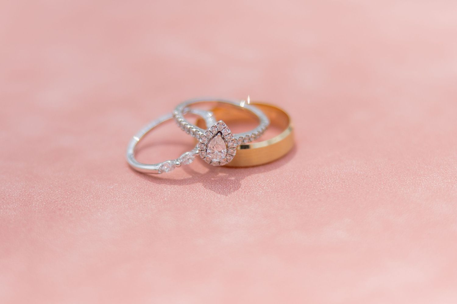 A delicate rose gold ring with a cushion cut diamond center stone against a pink background creates an elegant composition.