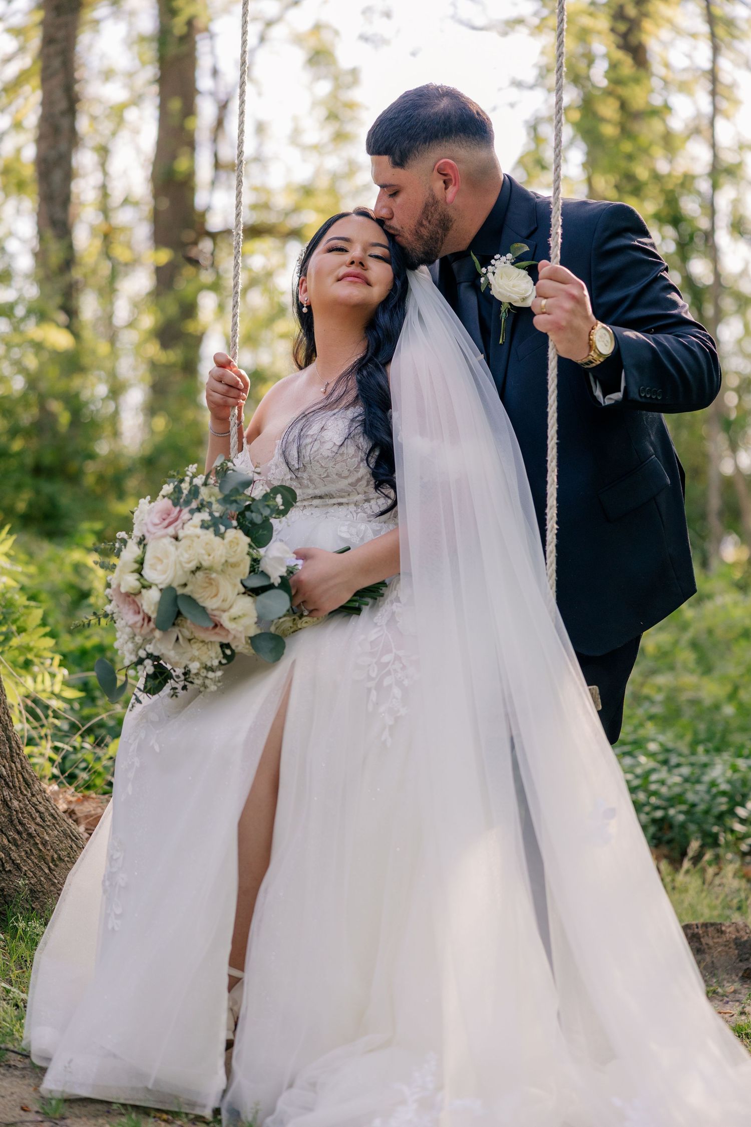 Newlyweds share intimate moments while taking photos in a wooded outdoor setting.