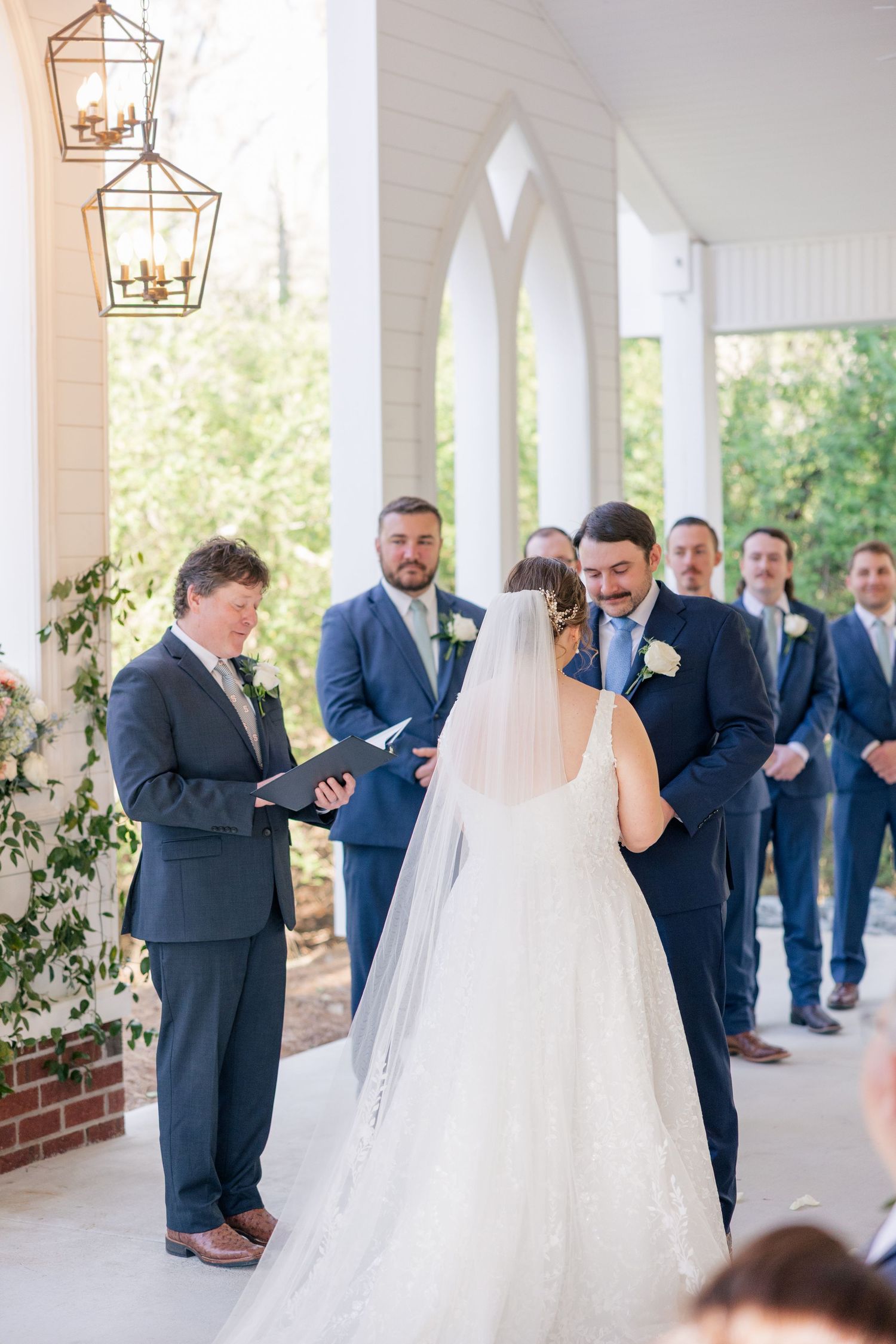 A series of shots showing a bridal party in navy suits and white veil in an elegant outdoor covered walkway.