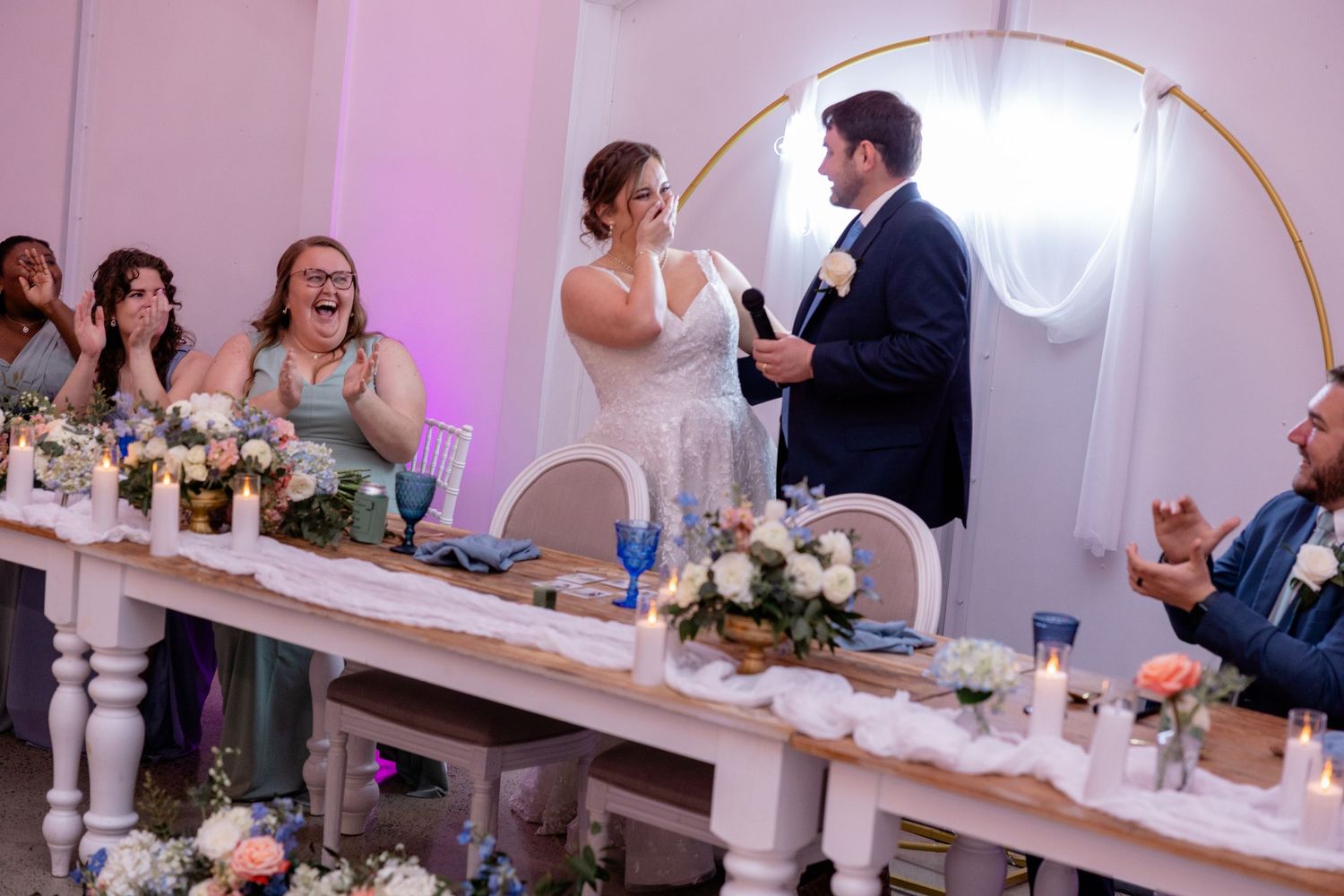 Wedding reception moment at decorated table with floral centerpieces and pink lighting.