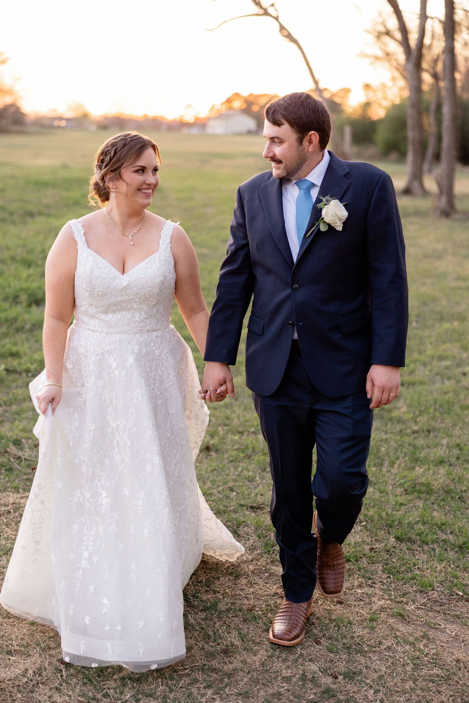 Wedding couple walking together on a grassy hill during golden hour, showcasing candid moments and joy.