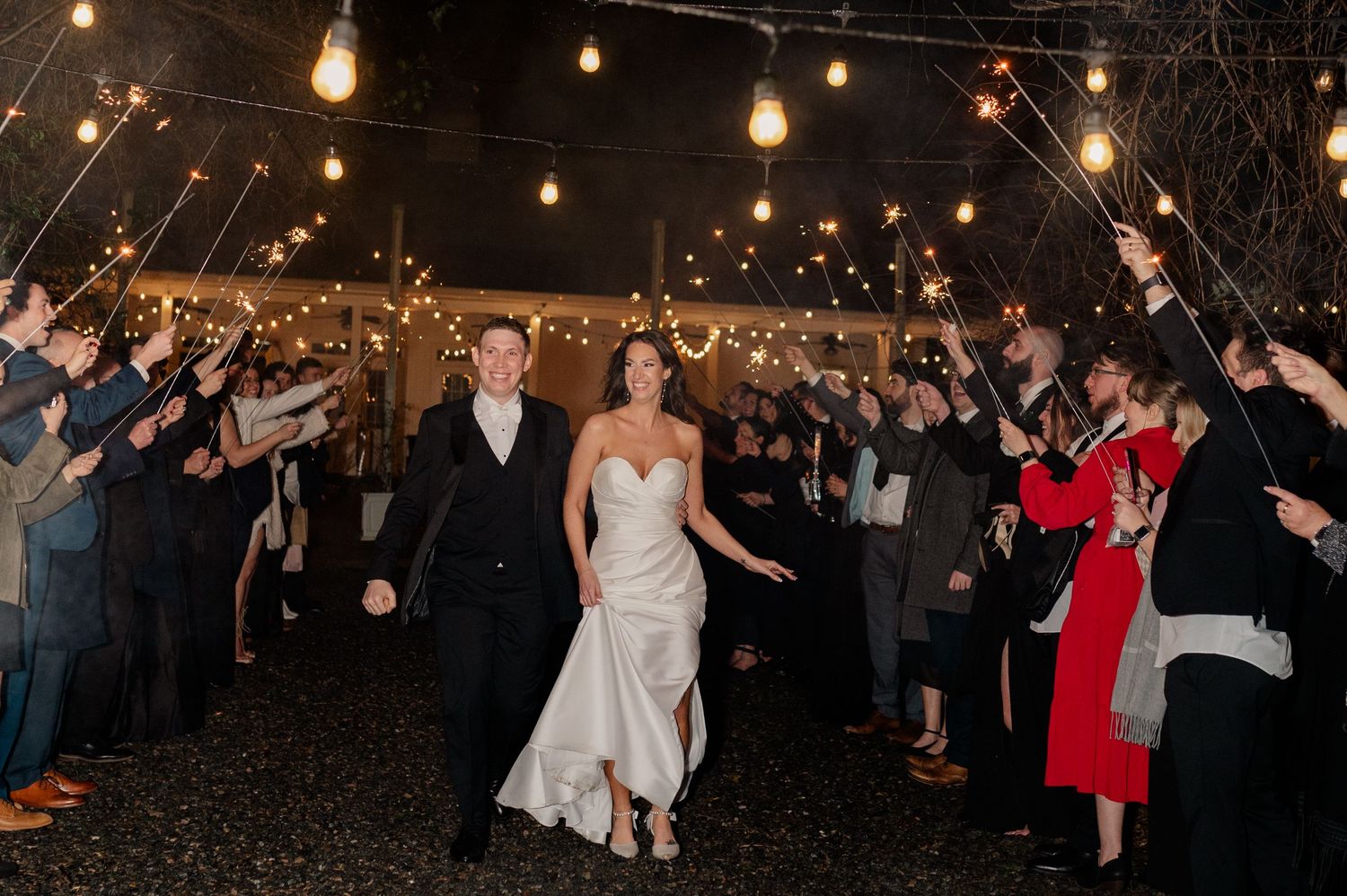 Wedding guests surround a happy couple on the dance floor while twirling sparklers during an evening celebration.