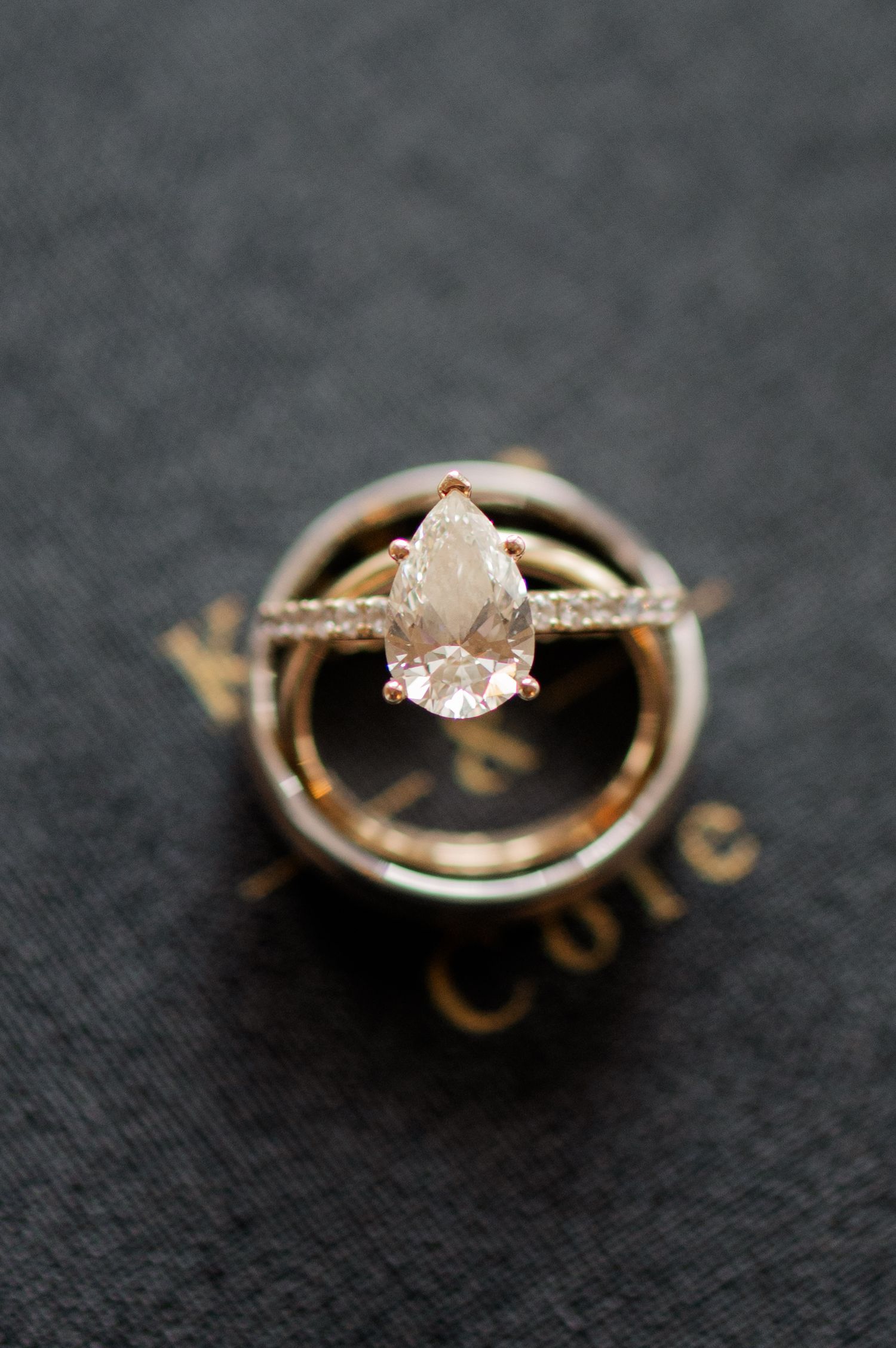Close-up macro photo sequence of rose gold engagement ring with pear shaped stone on dark fabric background.