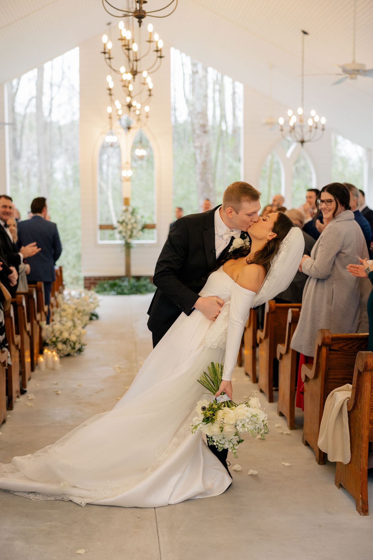 Romantic ceremony moments captured in a white chapel with large windows and beautiful natural lighting.