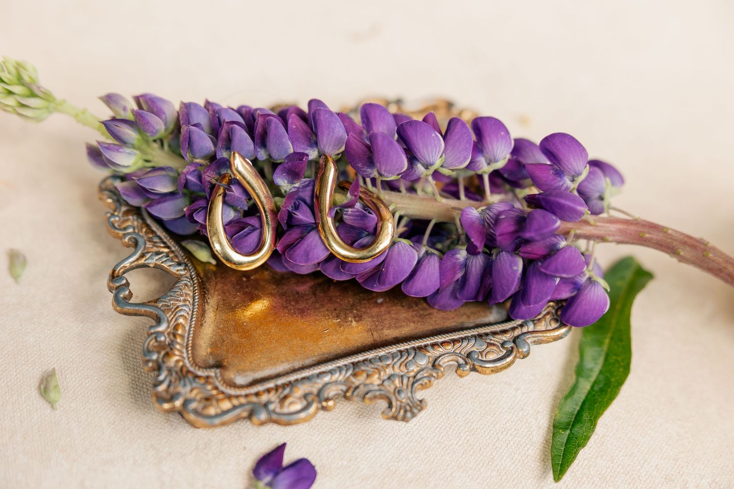 Gold teardrop earrings displayed on a vintage silver tray adorned with purple lupine flowers on a neutral background.