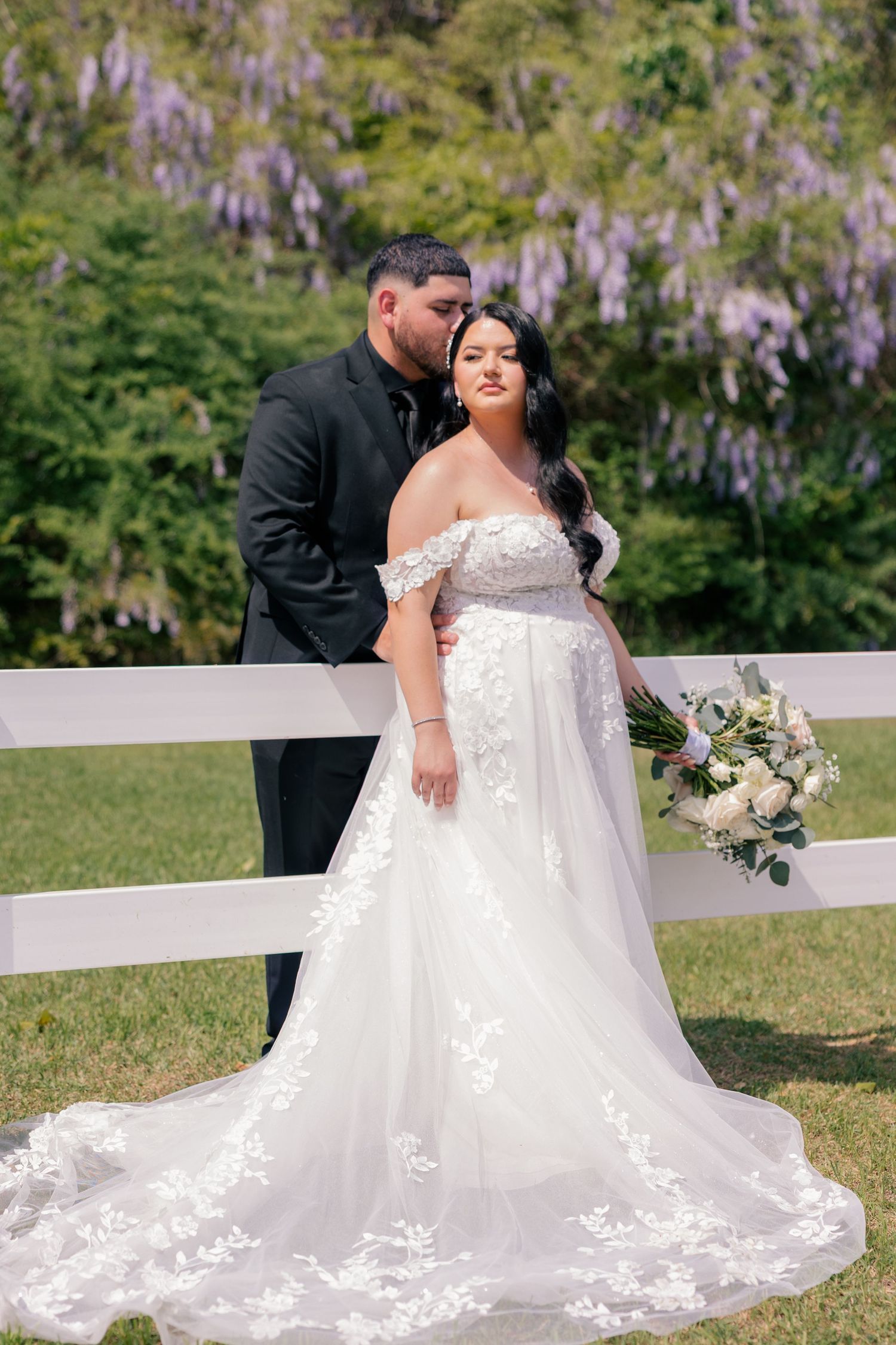 Beautiful wedding dress with lace details spreads across white fence during outdoor photo session.