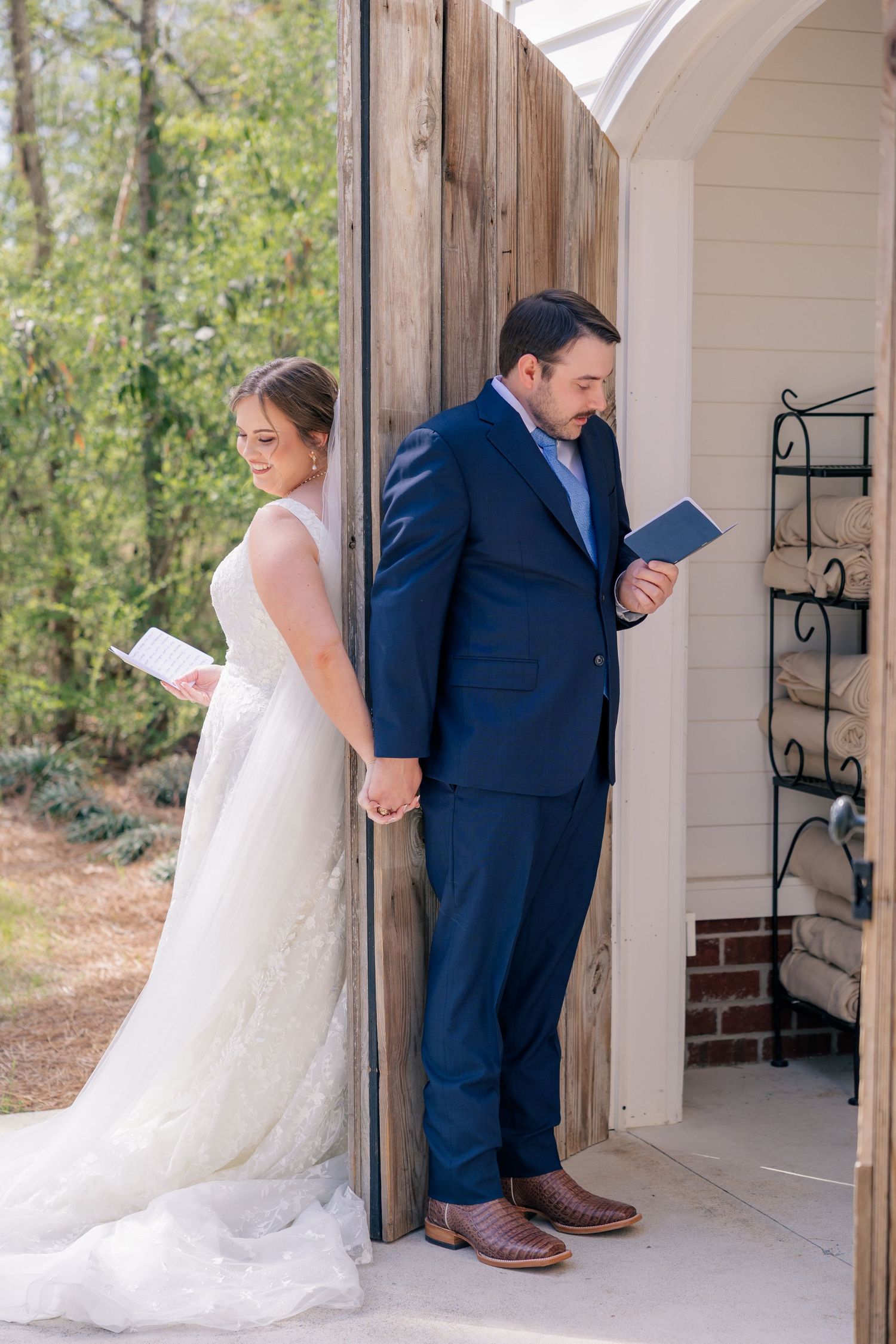 Wedding couple shares a private moment around a corner while holding letters at a white chapel.