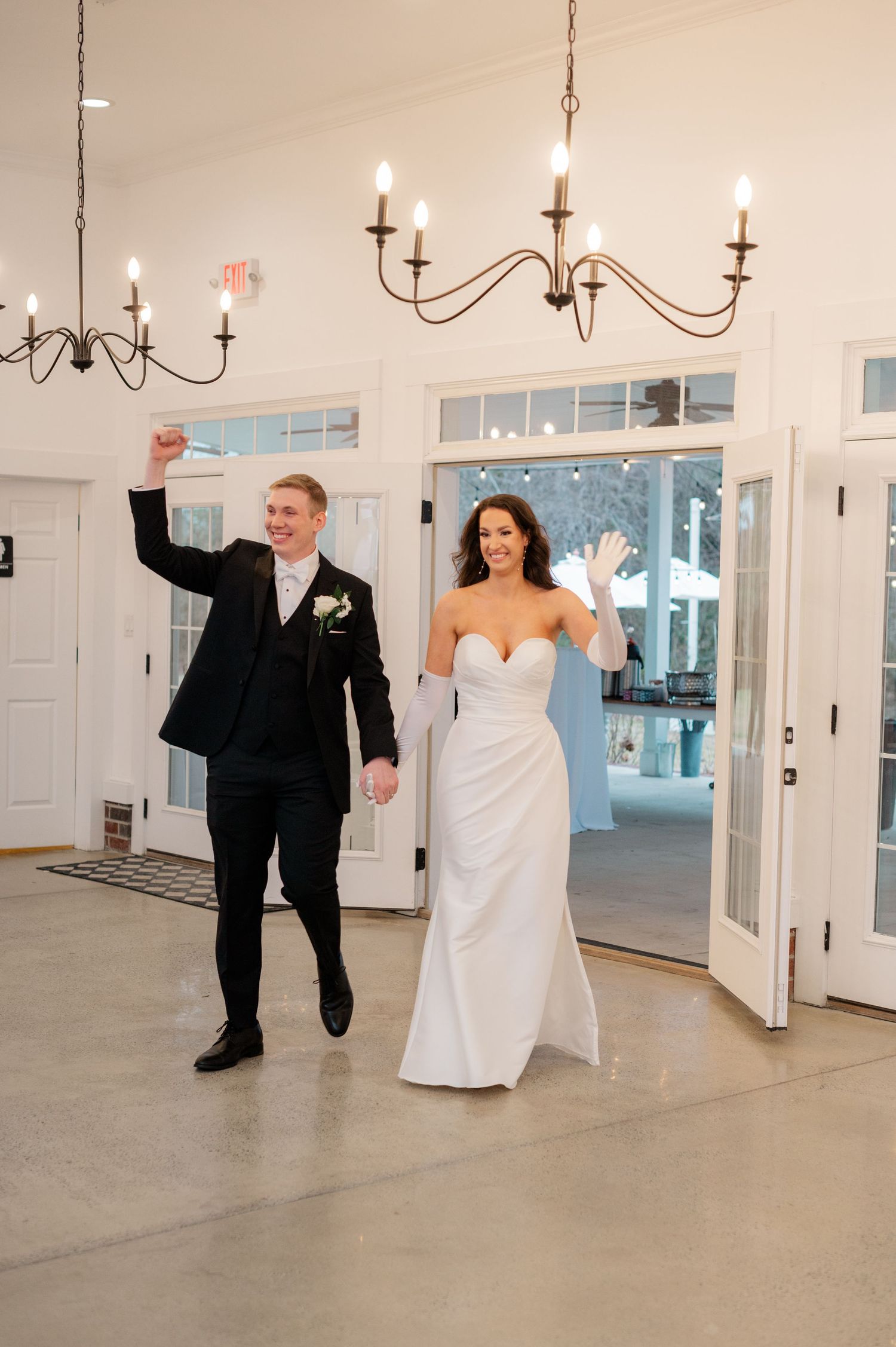 A joyful wedding celebration in a bright indoor venue with white walls and chandelier lighting.