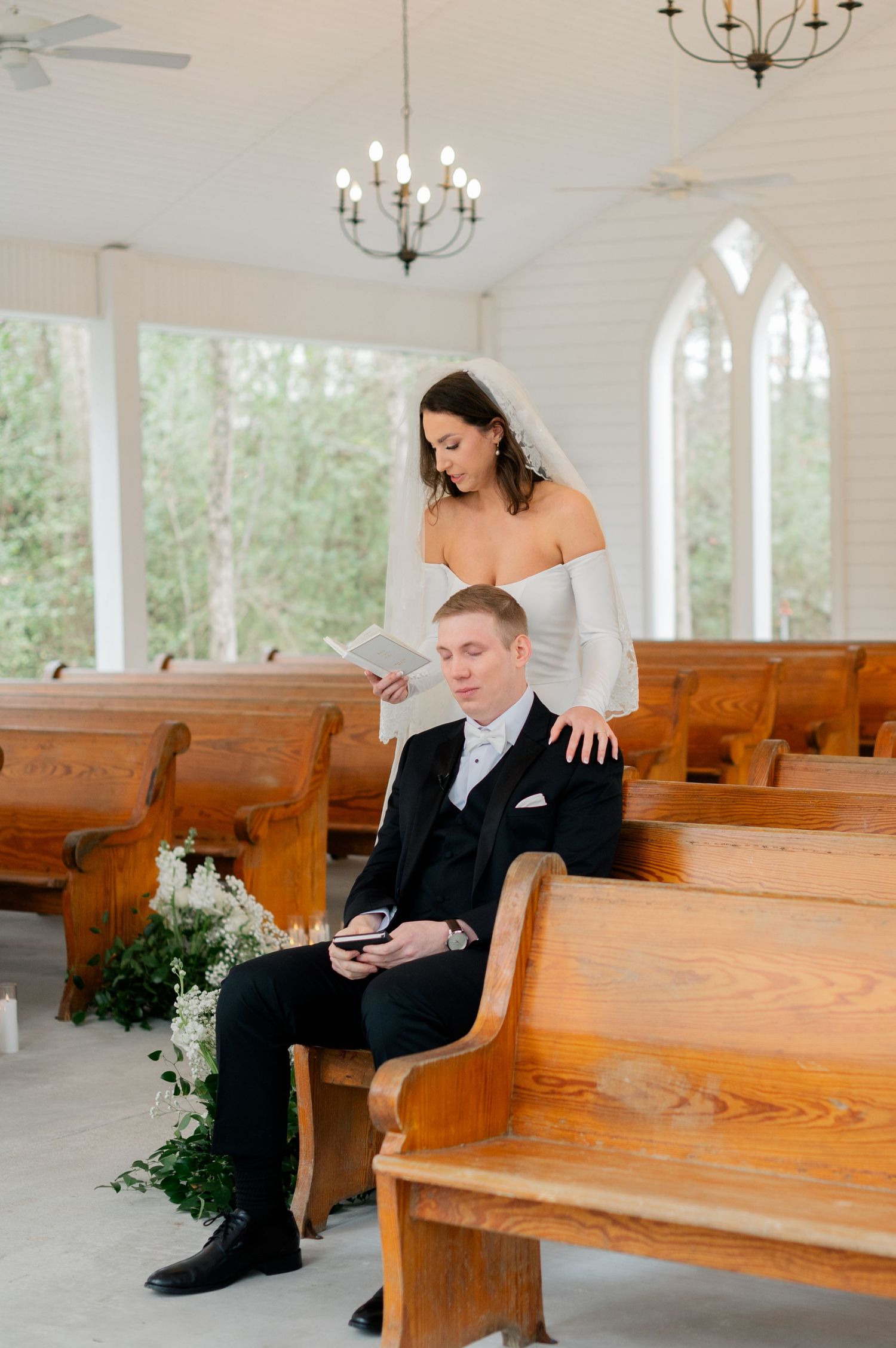 A couple shares a quiet moment together on wooden church pews before their wedding ceremony.