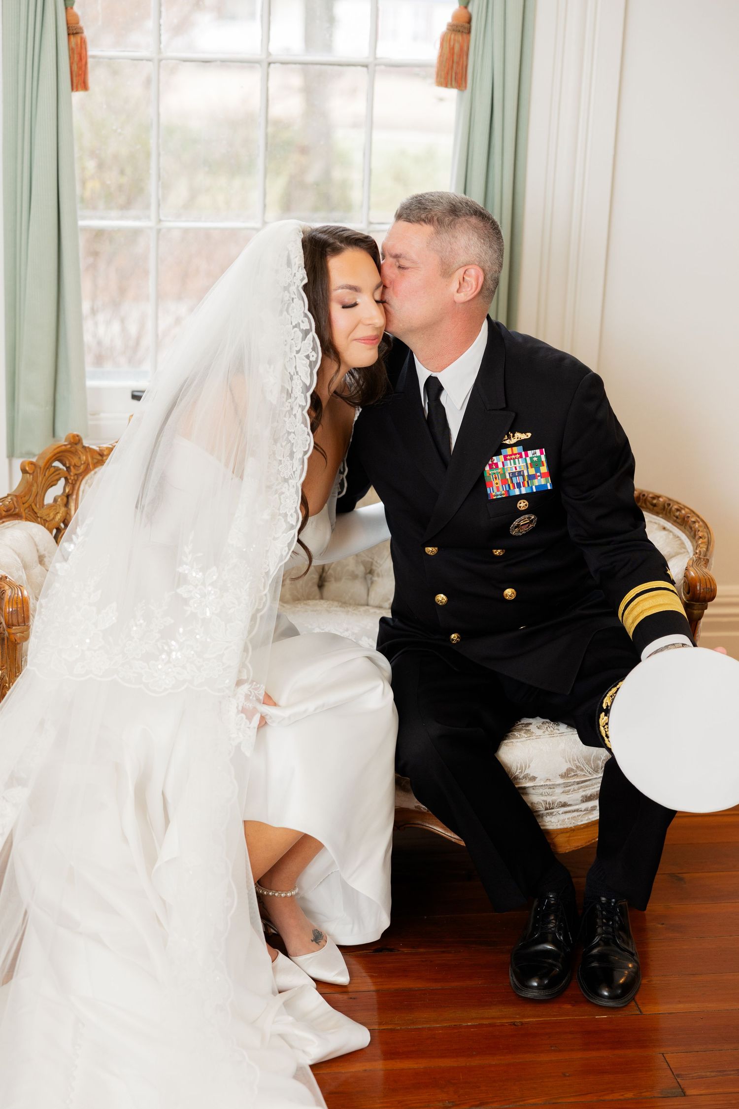 A touching wedding moment captured in white showing formal military attire against a bright interior setting.
