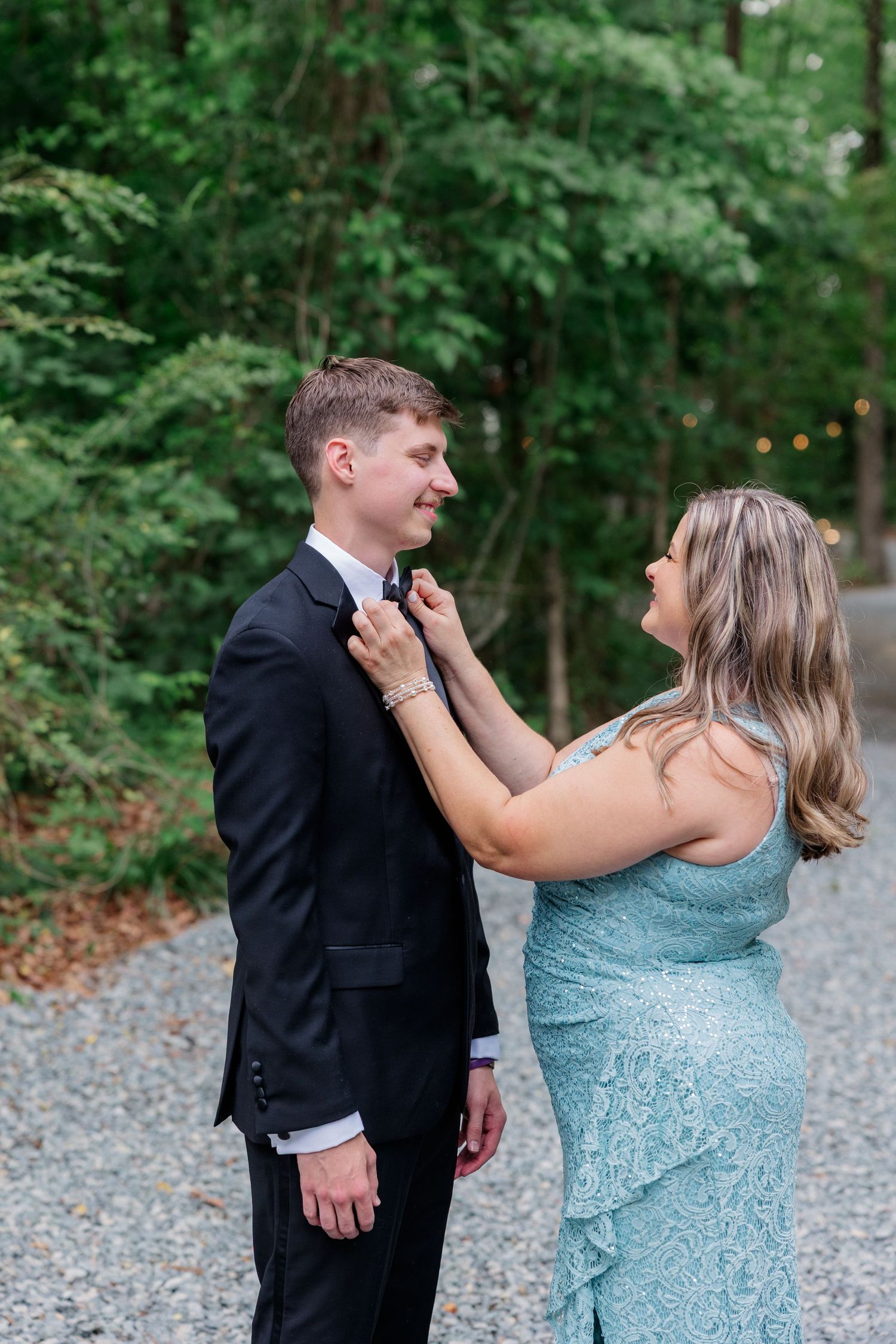A couple in formal attire dancing together outdoors amid green foliage.