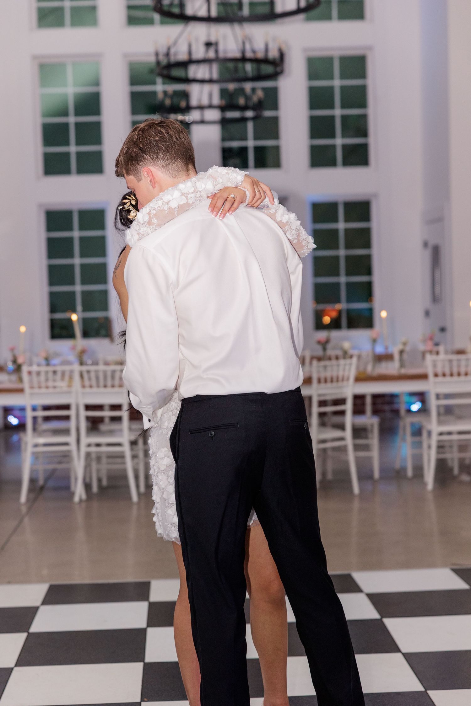 A couple shares an intimate dance moment on a black and white checkered floor in an elegant reception venue.