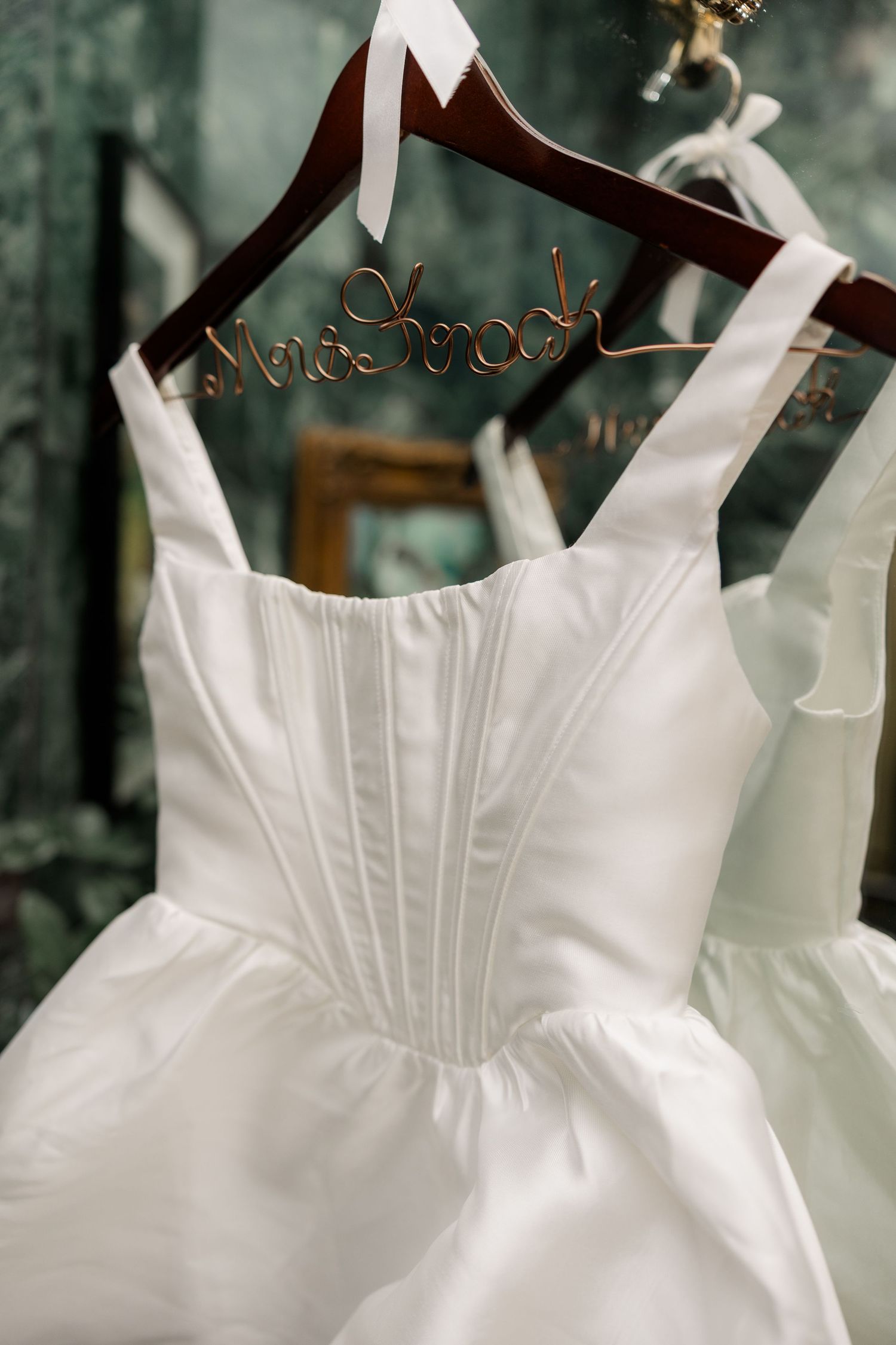 White wedding dress details showing pleated bodice and straps hanging on wooden hangers.