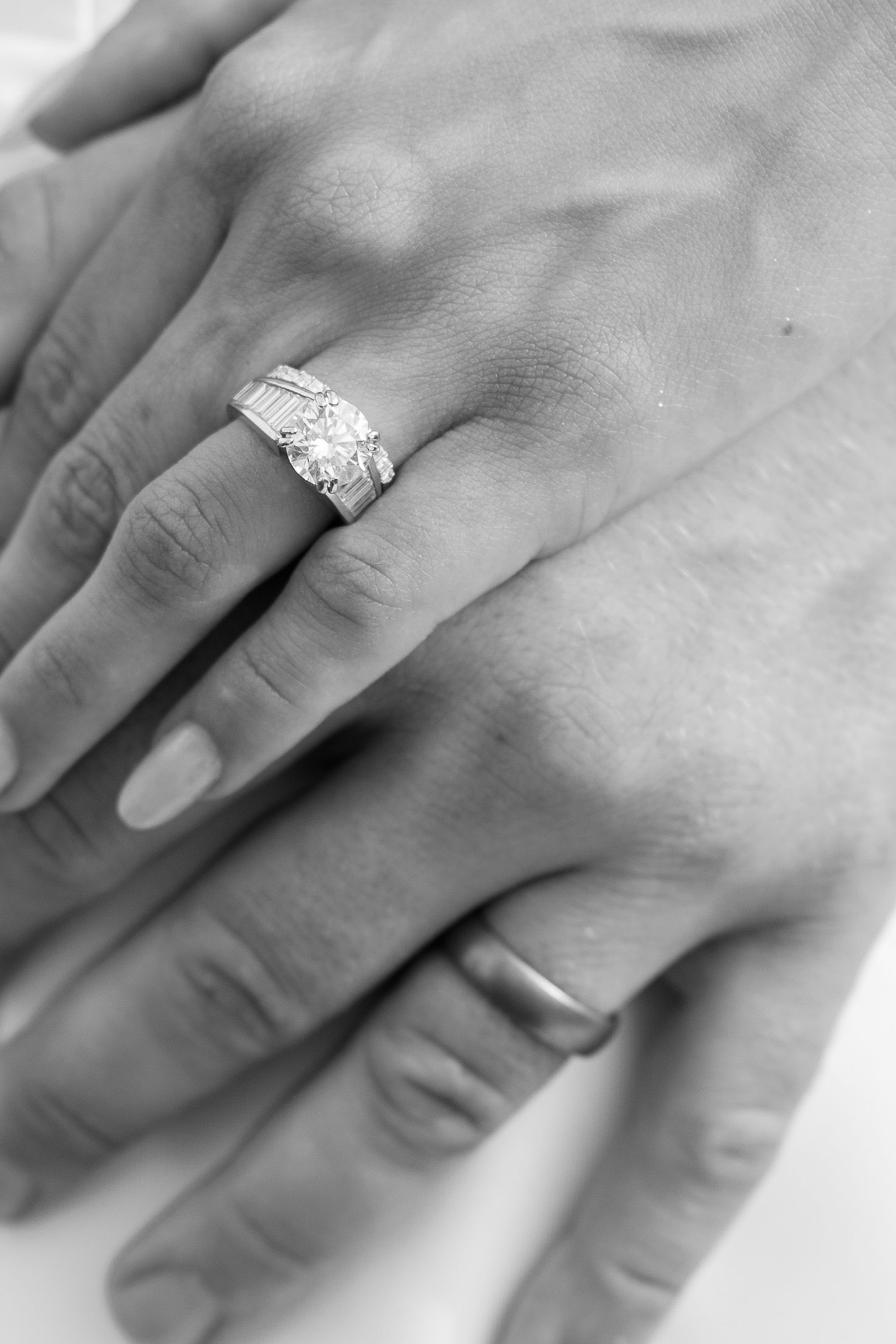 Close-up black and white photo of an ornate diamond engagement ring on a woman's hand.