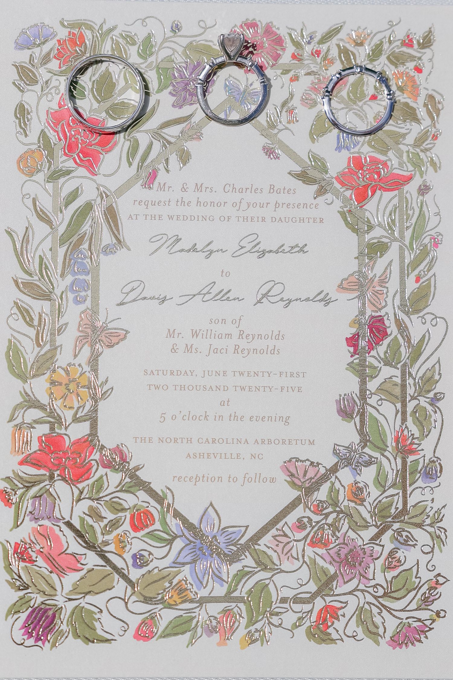 Floral wedding invitation with ornate botanical border and three rings photographed from above.