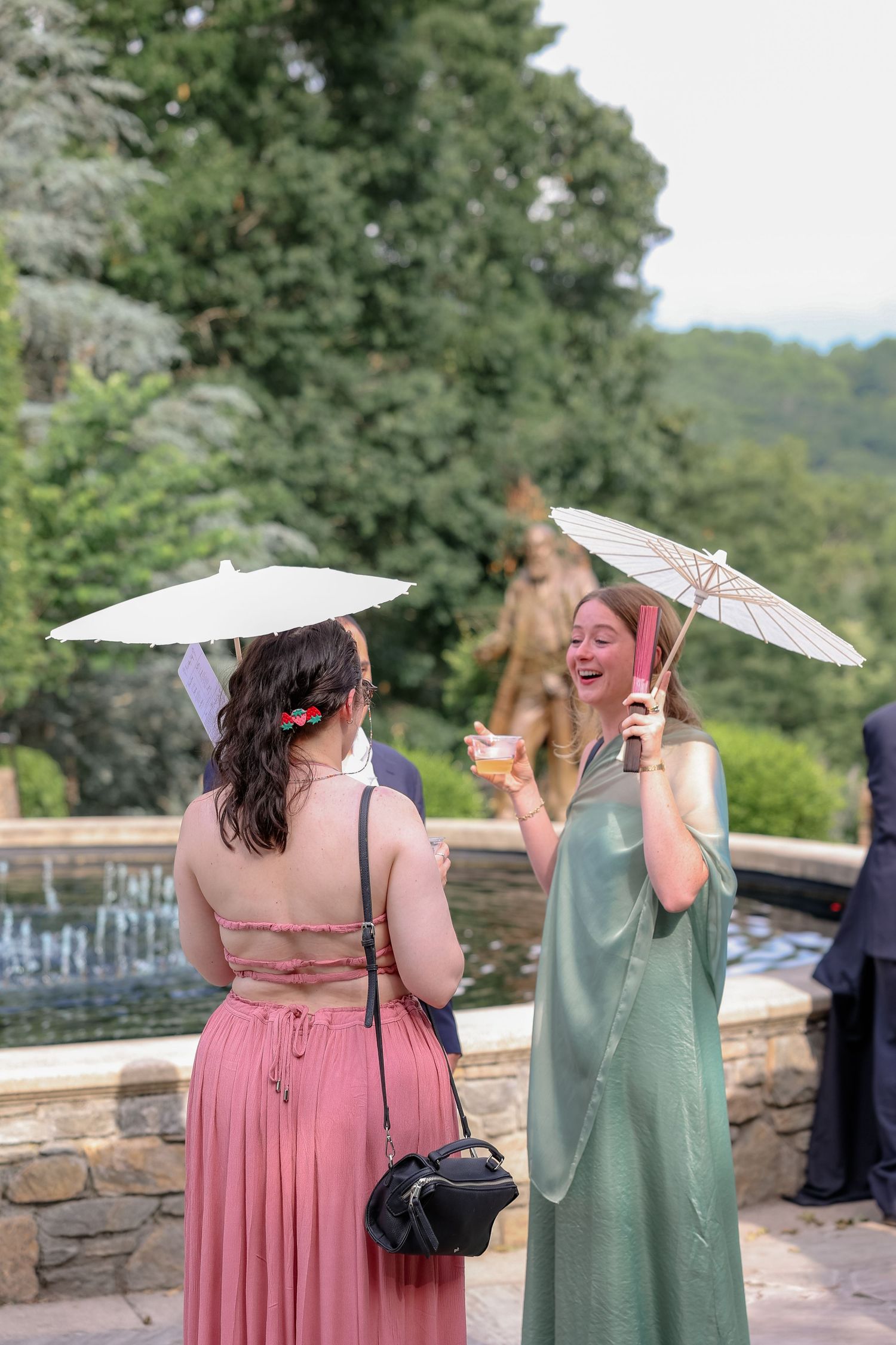 Two guests with parasols share a joyful moment at an outdoor event.