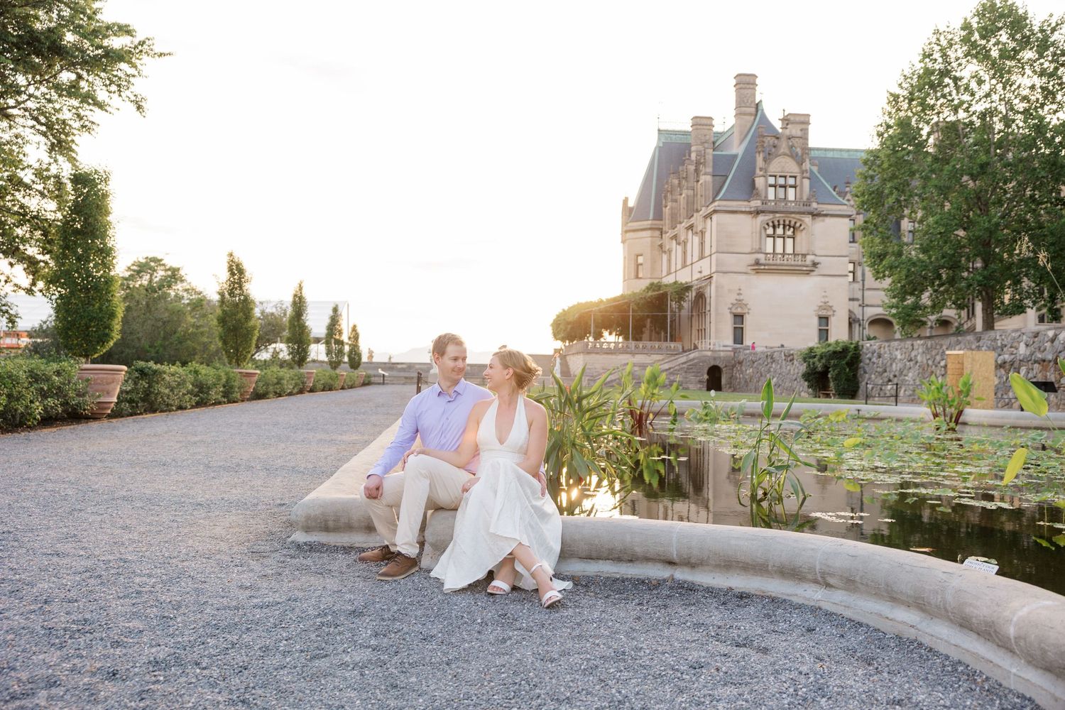 A couple sits together on stone steps at a romantic European estate during golden hour sunset.