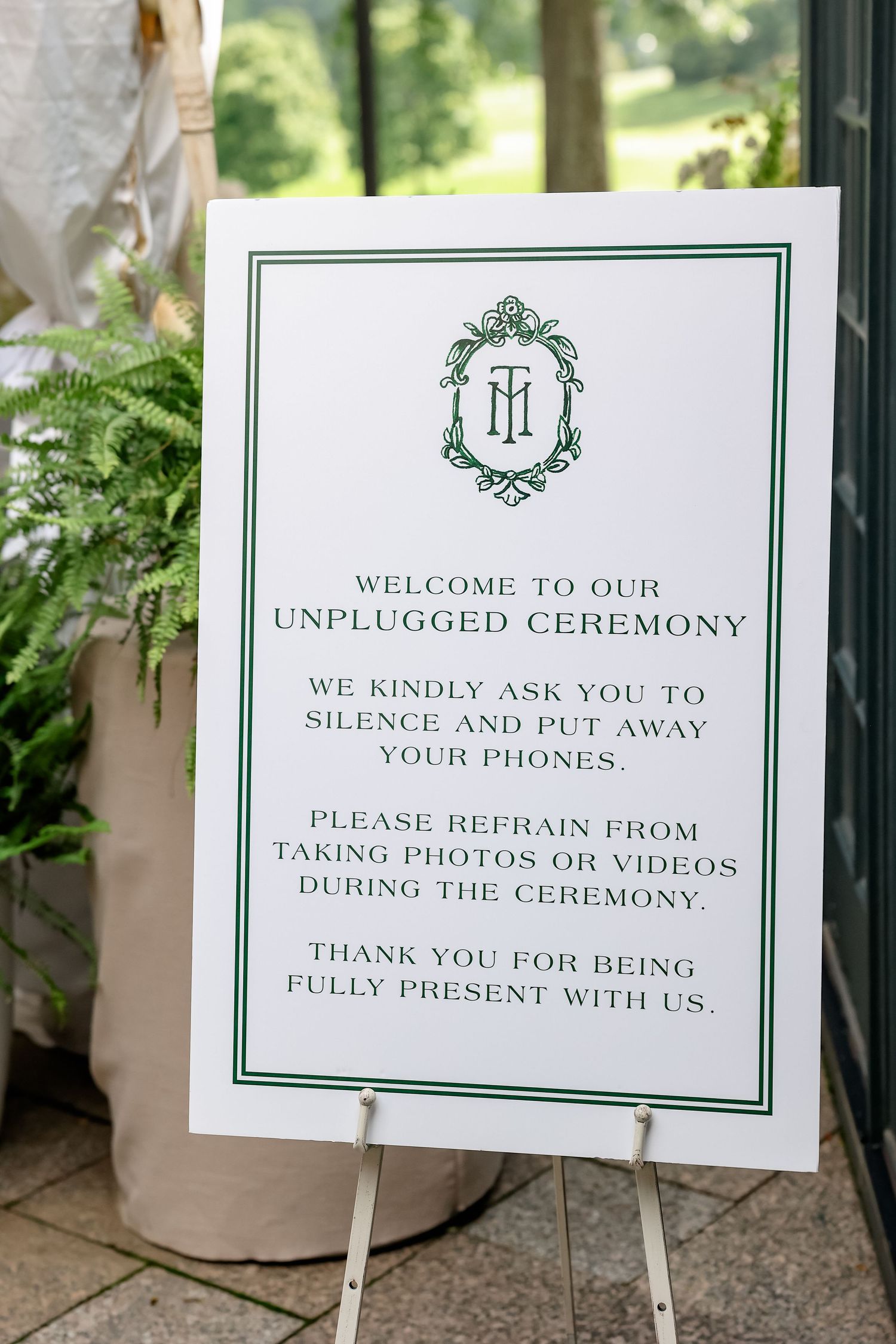 Elegant white wedding unplugged ceremony sign on easel requesting guests silence phones during the ceremony.