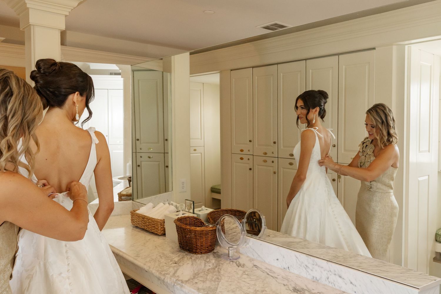 Elegant bridal preparation scene reflected in mirror with white wedding gown and getting ready details in cream-colored room.