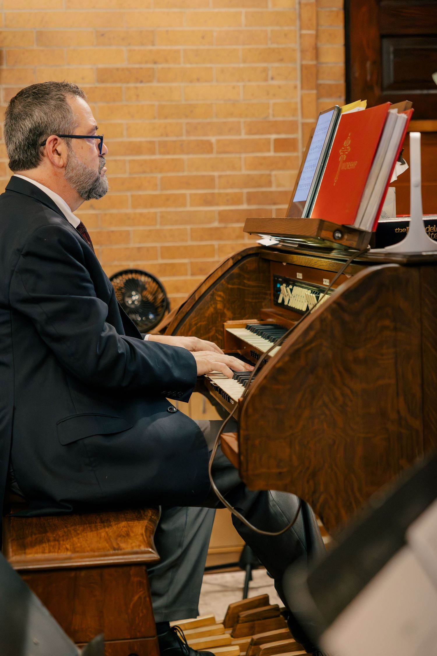 Musician plays a classic wooden organ during a wedding ceremony in a brick-walled church setting.