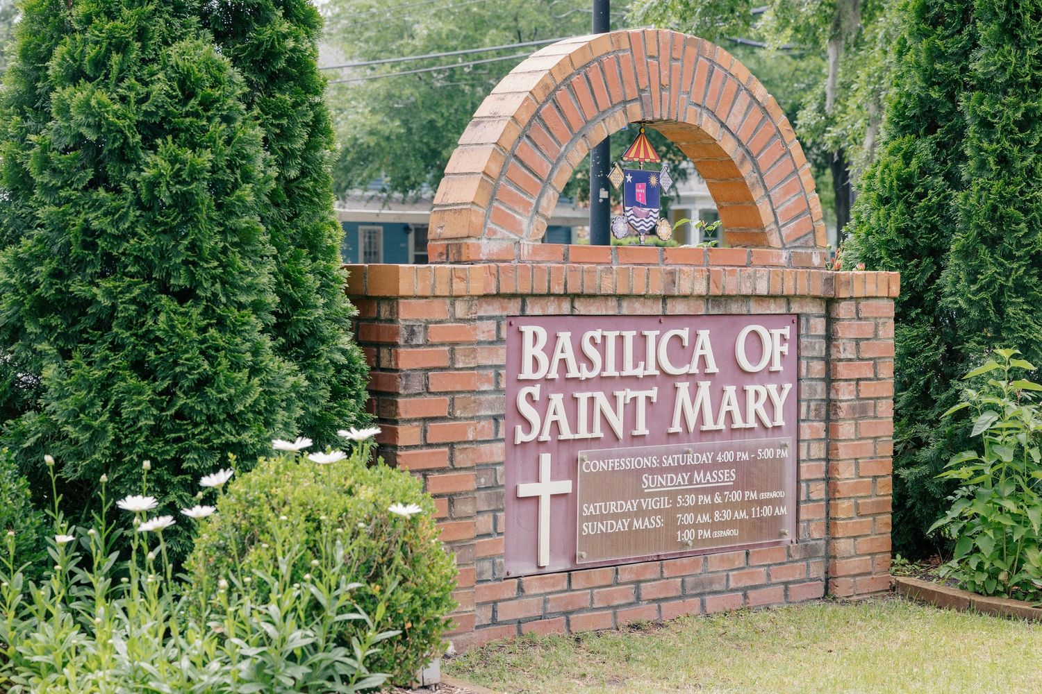 Brick entrance sign for the Basilica of Saint Mary surrounded by lush green trees and shrubs.