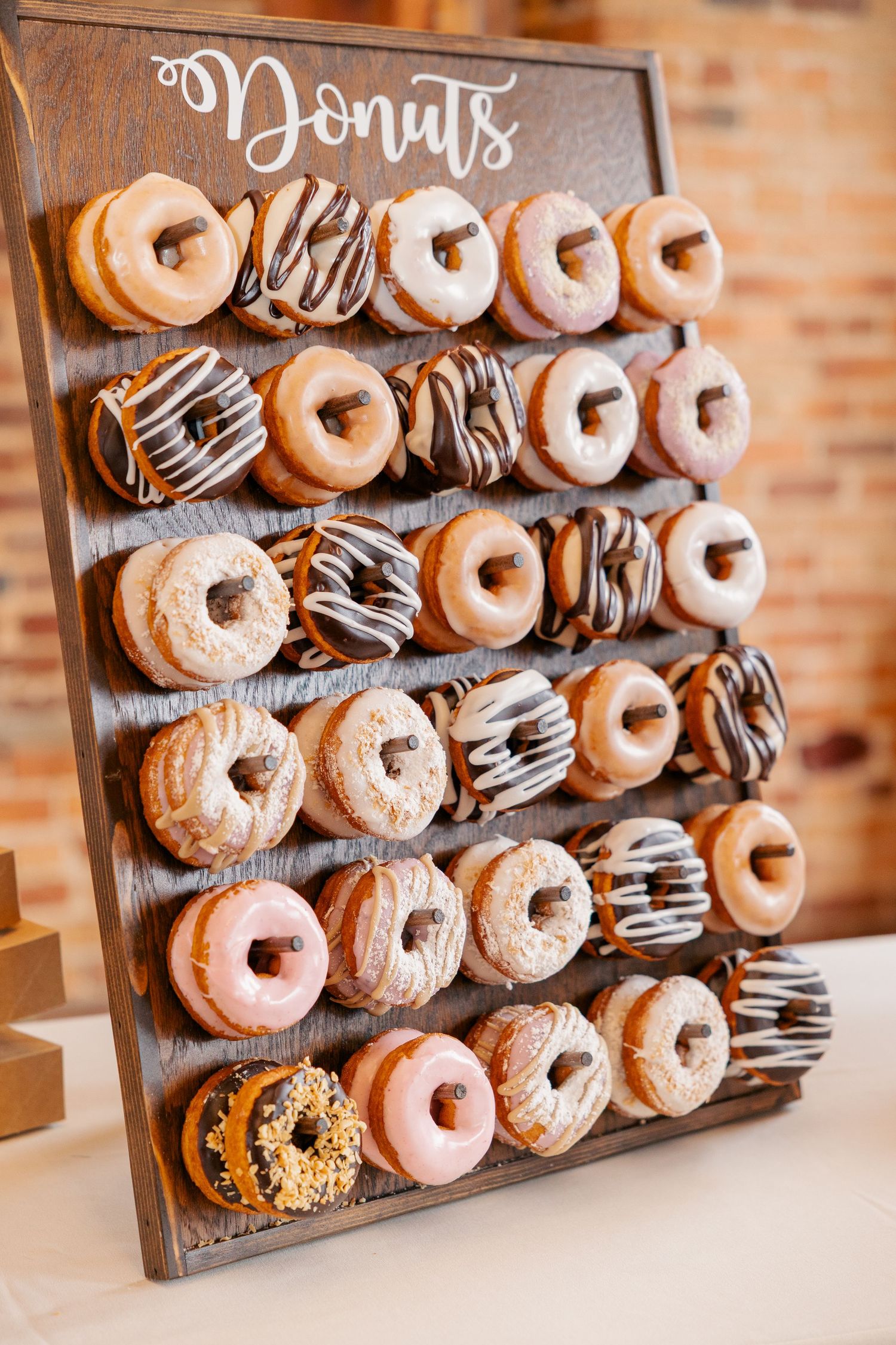Rustic wooden donut wall display filled with assorted glazed donuts at wedding reception dessert station.