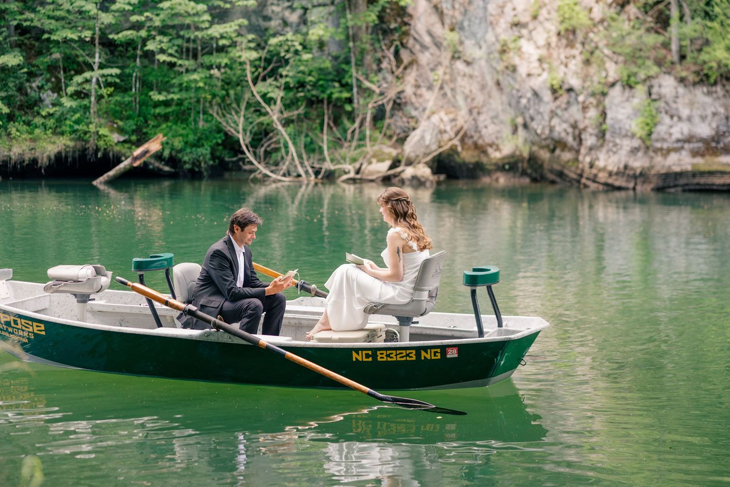 Bride and groom sitting in a green canoe on a serene green lake surrounded by lush forest on their wedding day.