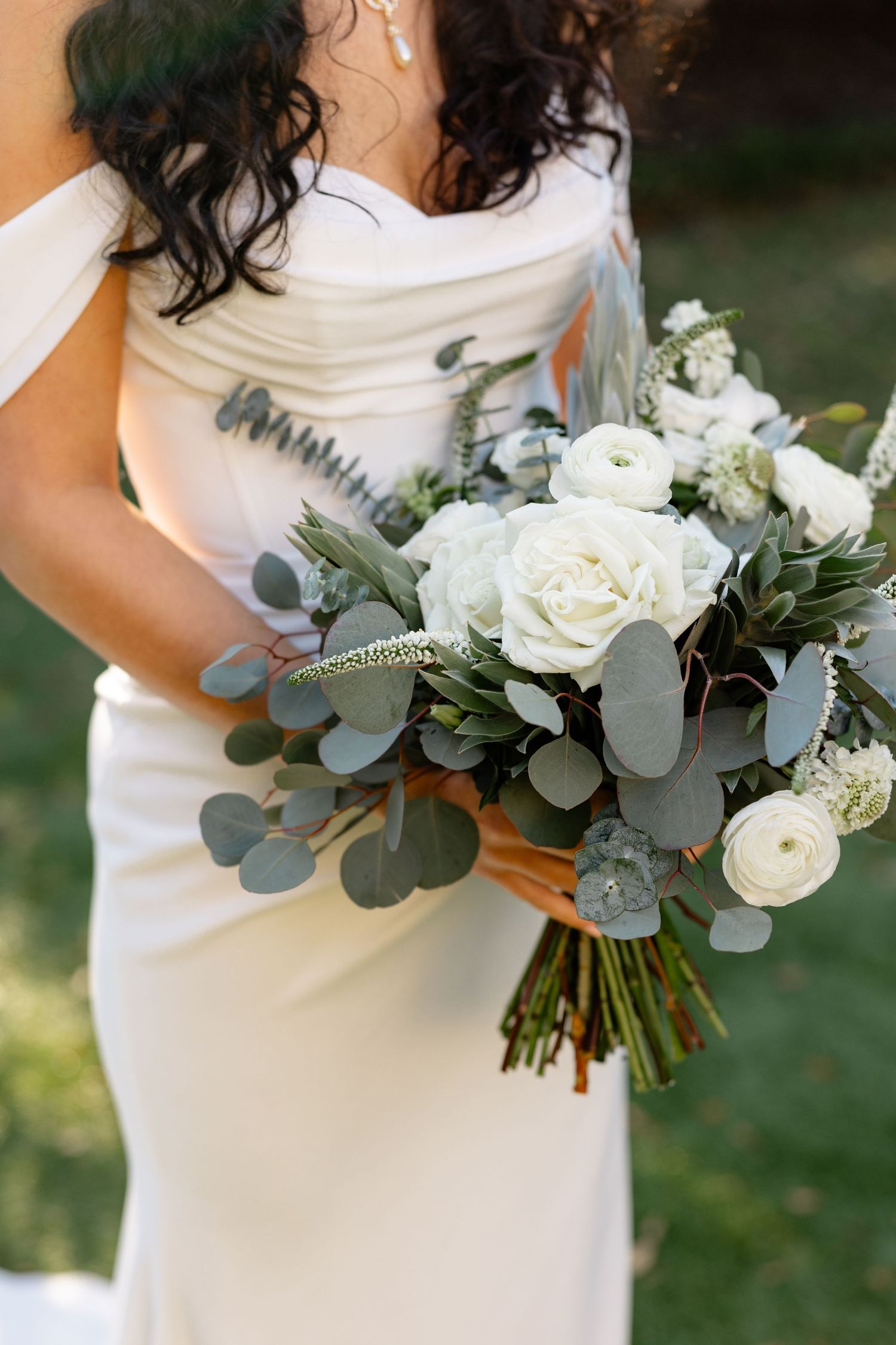 Bride holding romantic white and eucalyptus wedding bouquet with roses and greenery.