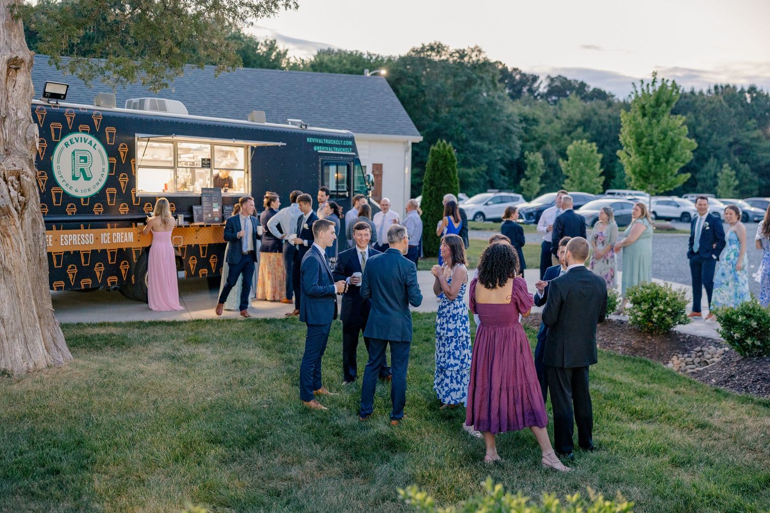 Wedding guests mingle outdoors near food truck at summer evening wedding reception.
