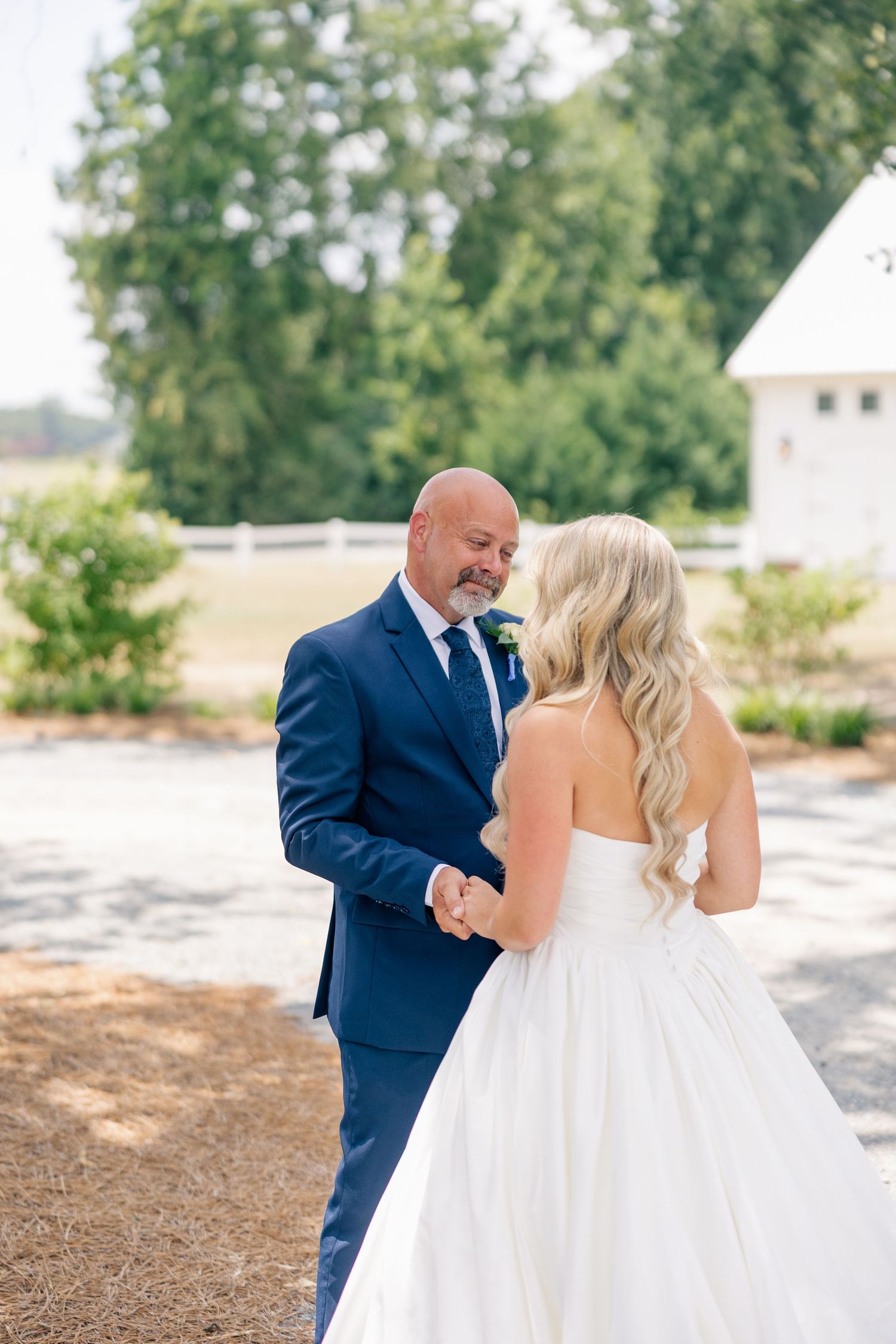 Emotional father sees bride daughter in white strapless gown for first look near white barn venue.