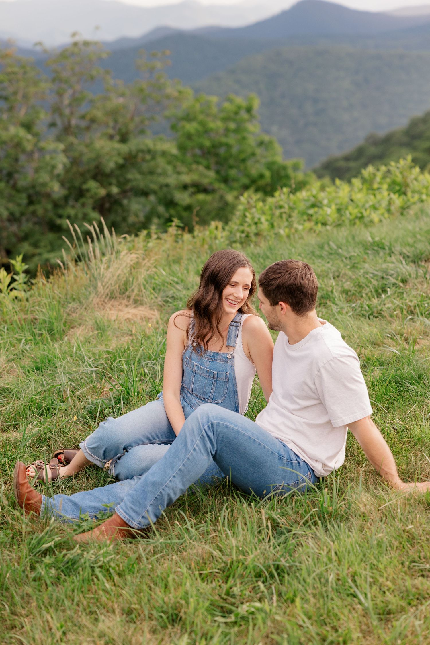 Couple relaxing together on a grassy hillside with mountains in the background.