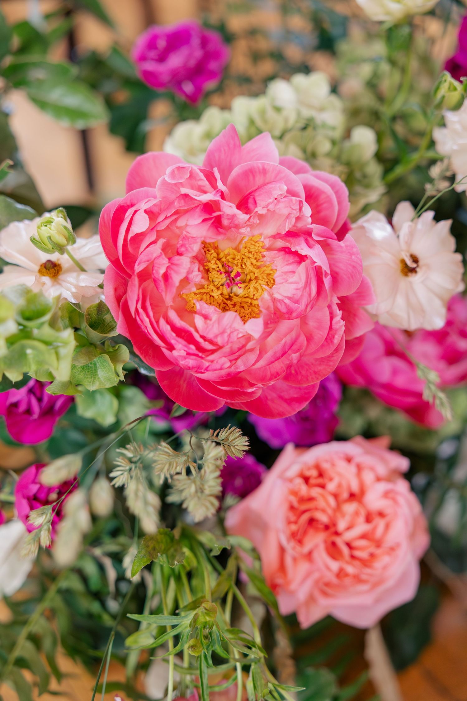 Close-up of vibrant pink peony and rose wedding bouquet with lush green foliage.
