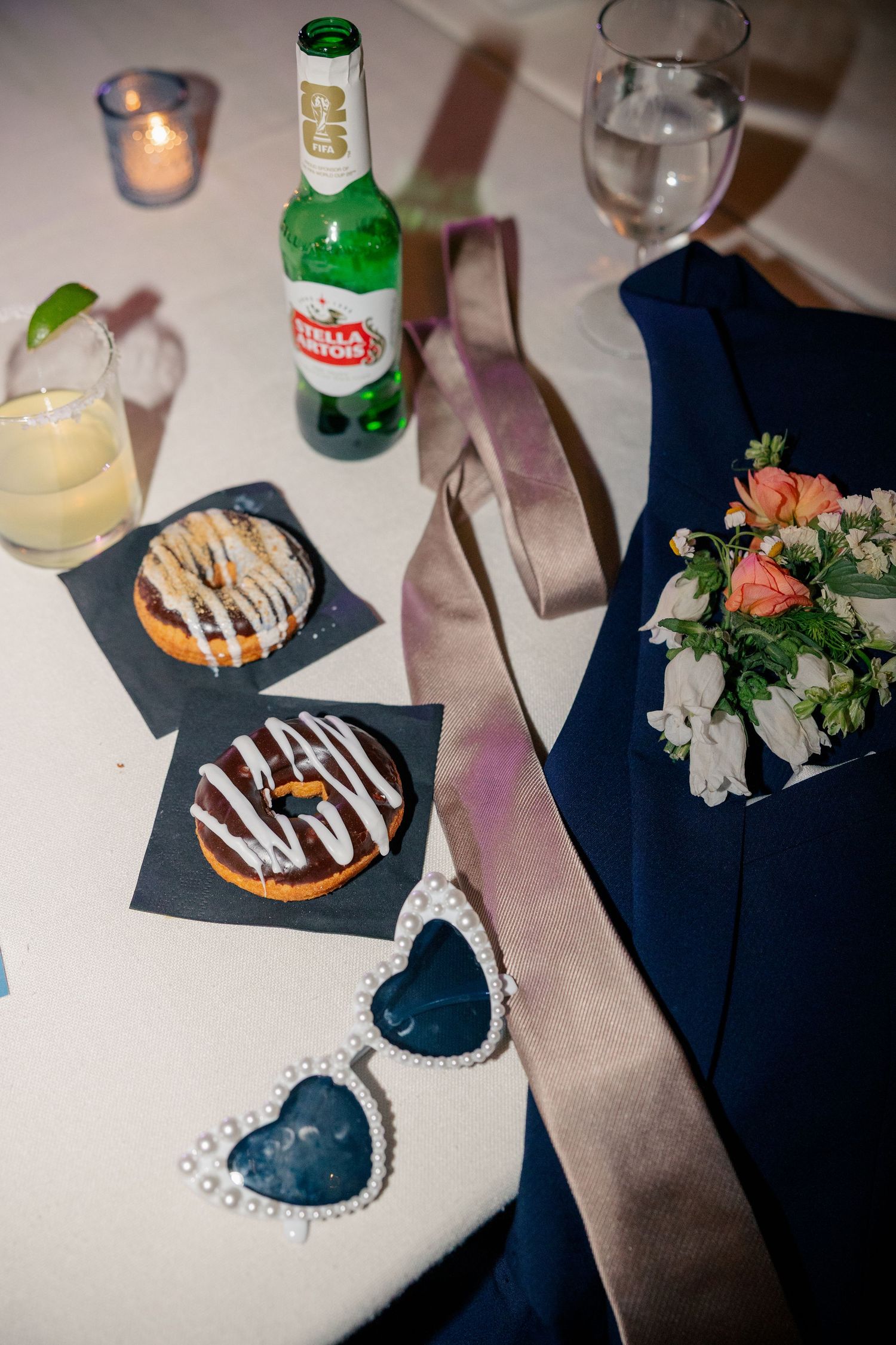 Wedding reception table detail with donuts, Stella Artois beer, heart sunglasses, boutonniere, and cocktails.